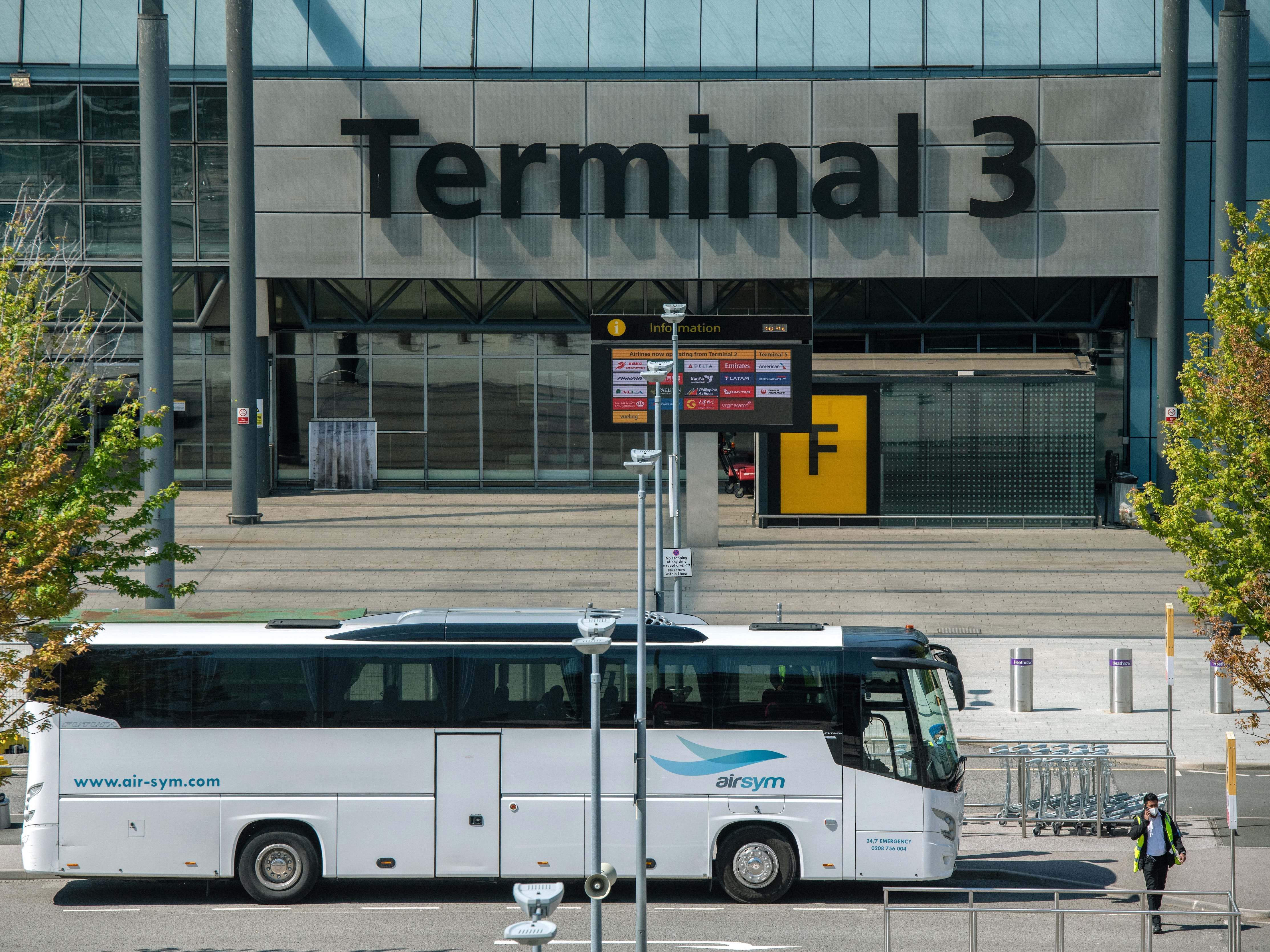 A bus used to transport red list arriving airline passengers passes Heathrow Terminal 3 building at Heathrow Airport