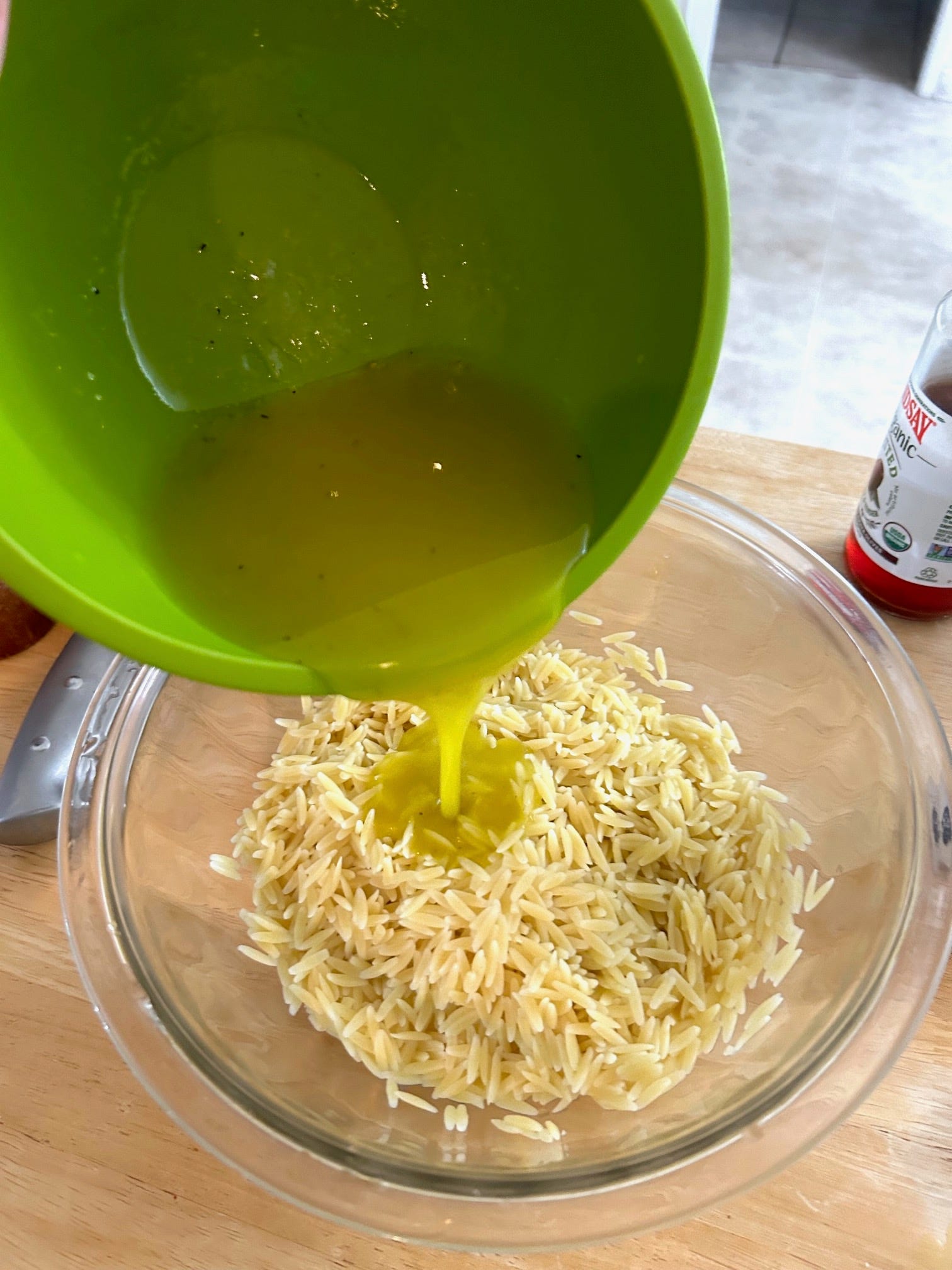 Pouring the dressing onto the orzo for Ina Garten's Greek Orzo Salad