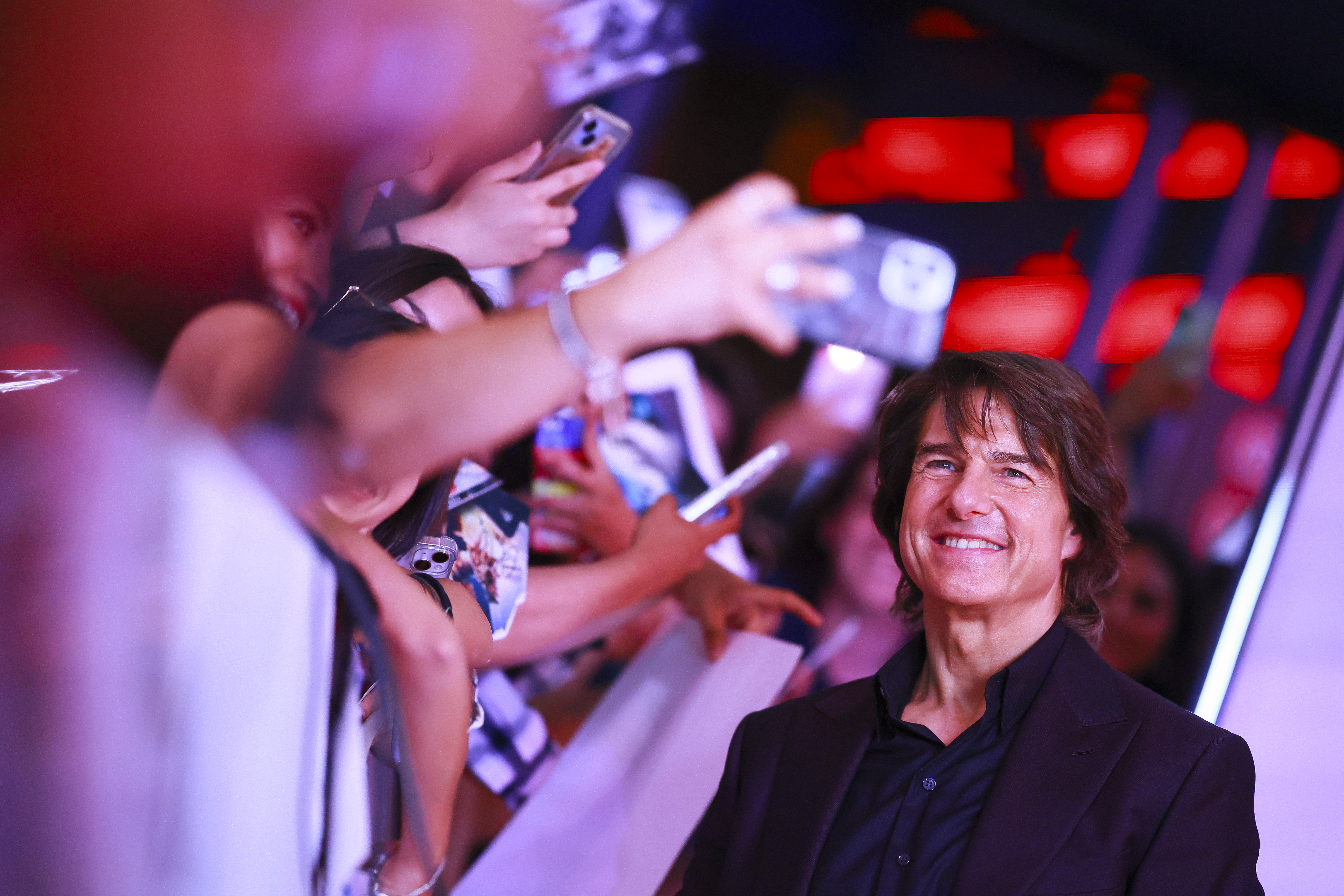 Tom Cruise smiles for fan photos at an event. 