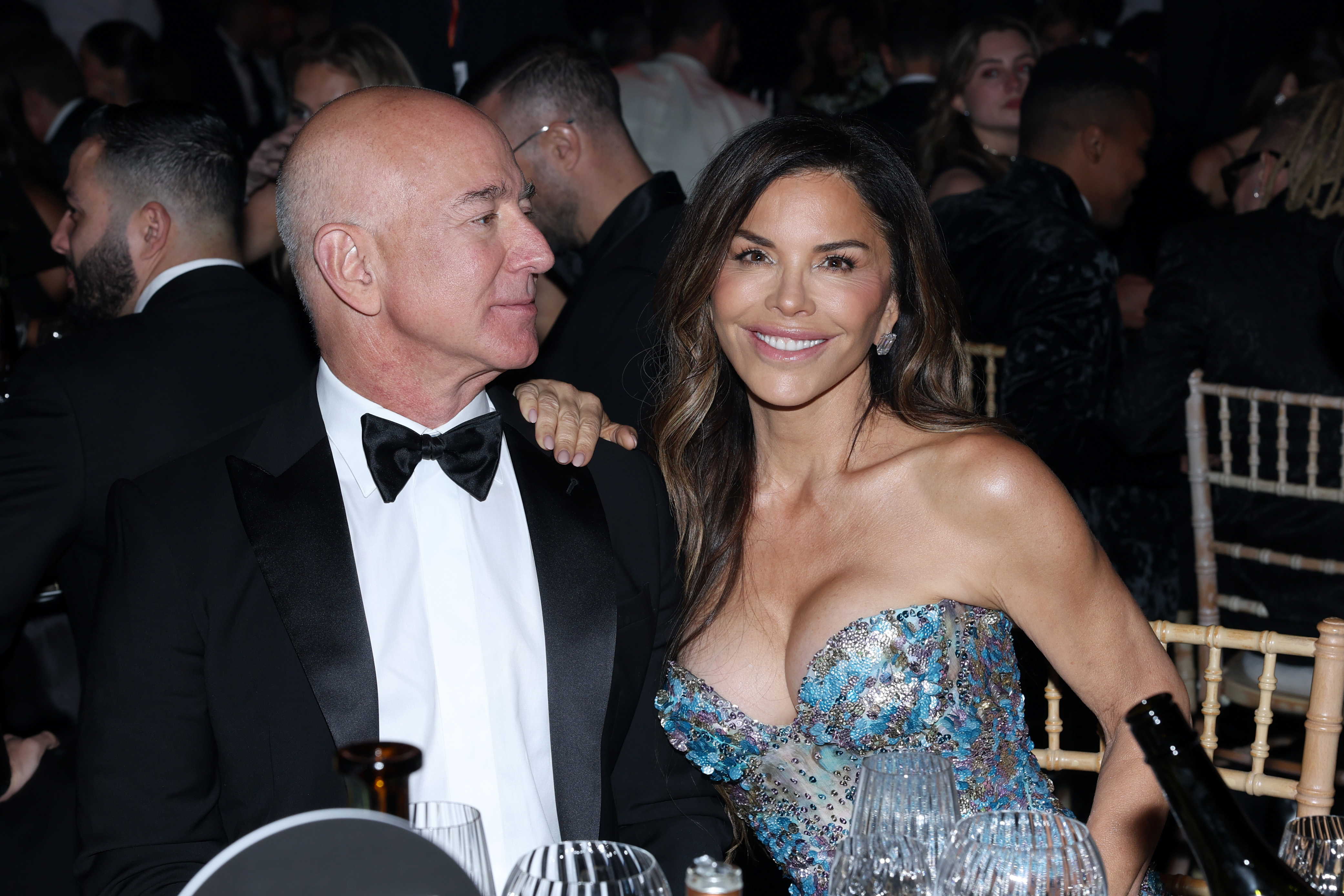Lauren Sánchez and Jeff Bezos smile at a formal dinner table. 