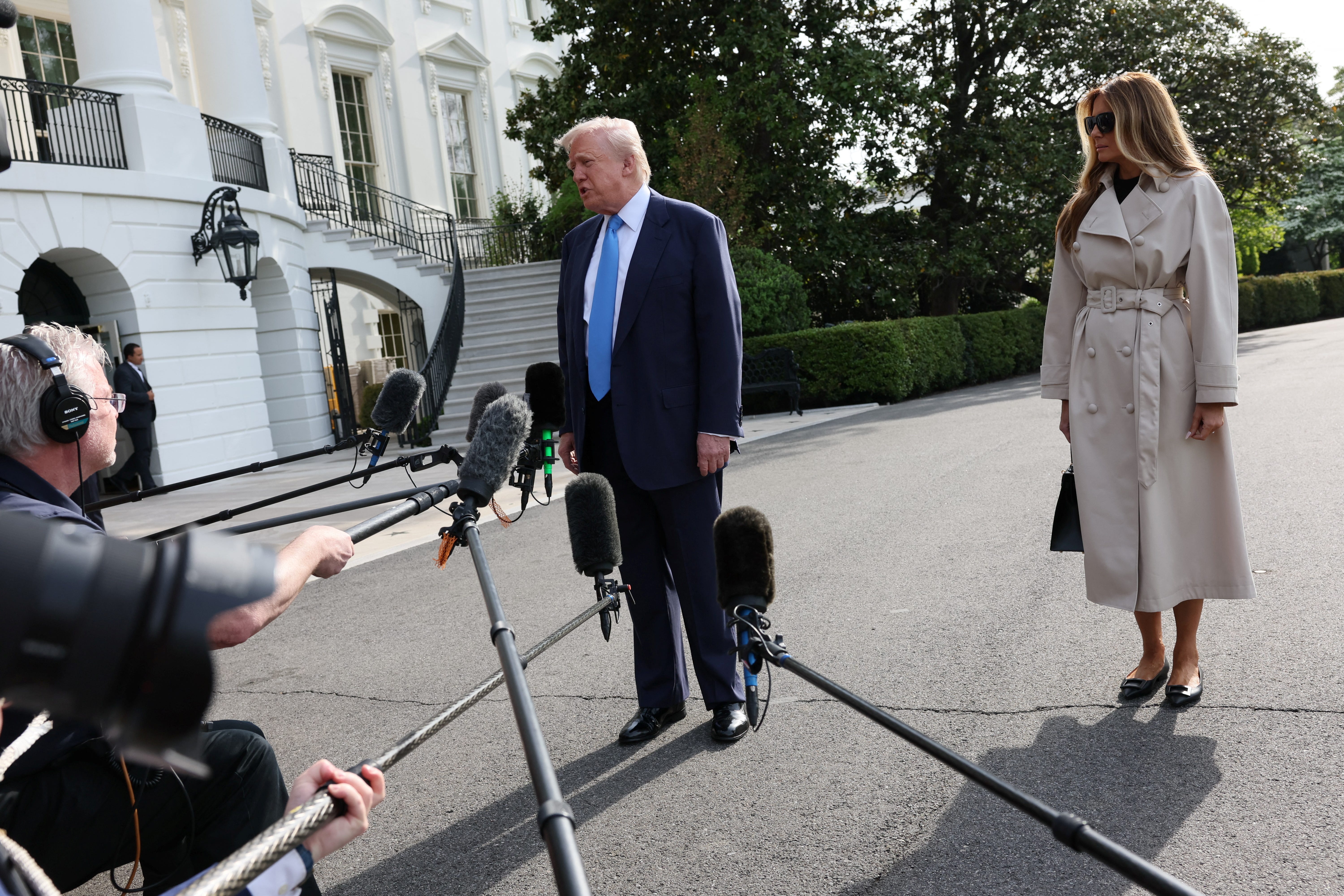 Donald Trump speaks to the press as Melania Trump stands in the background.