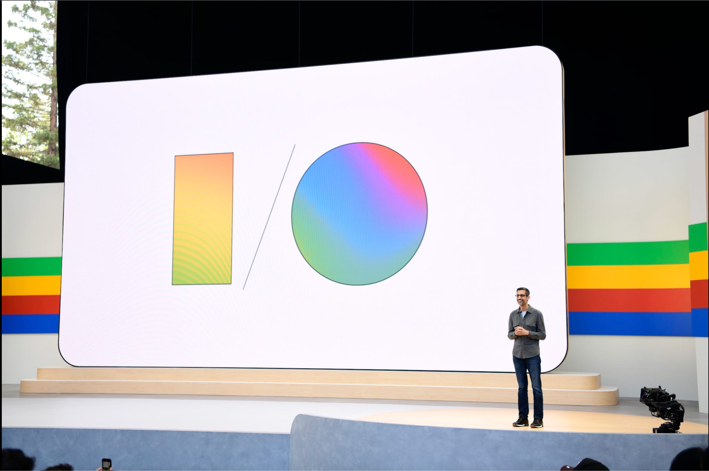 Google CEO Sundar Pichai speaks on a stage, in front of a large screen with the Google I/O logo in rainbow colors, during the company's annual developer conference.