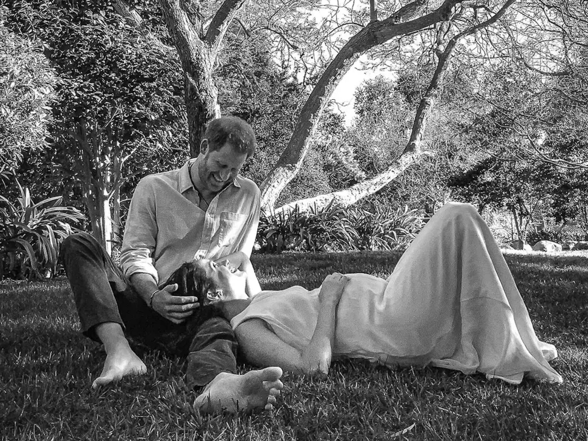 A black-and-white photo shows Prince Harry looking down at a pregnant Meghan Markle lying in his lap.