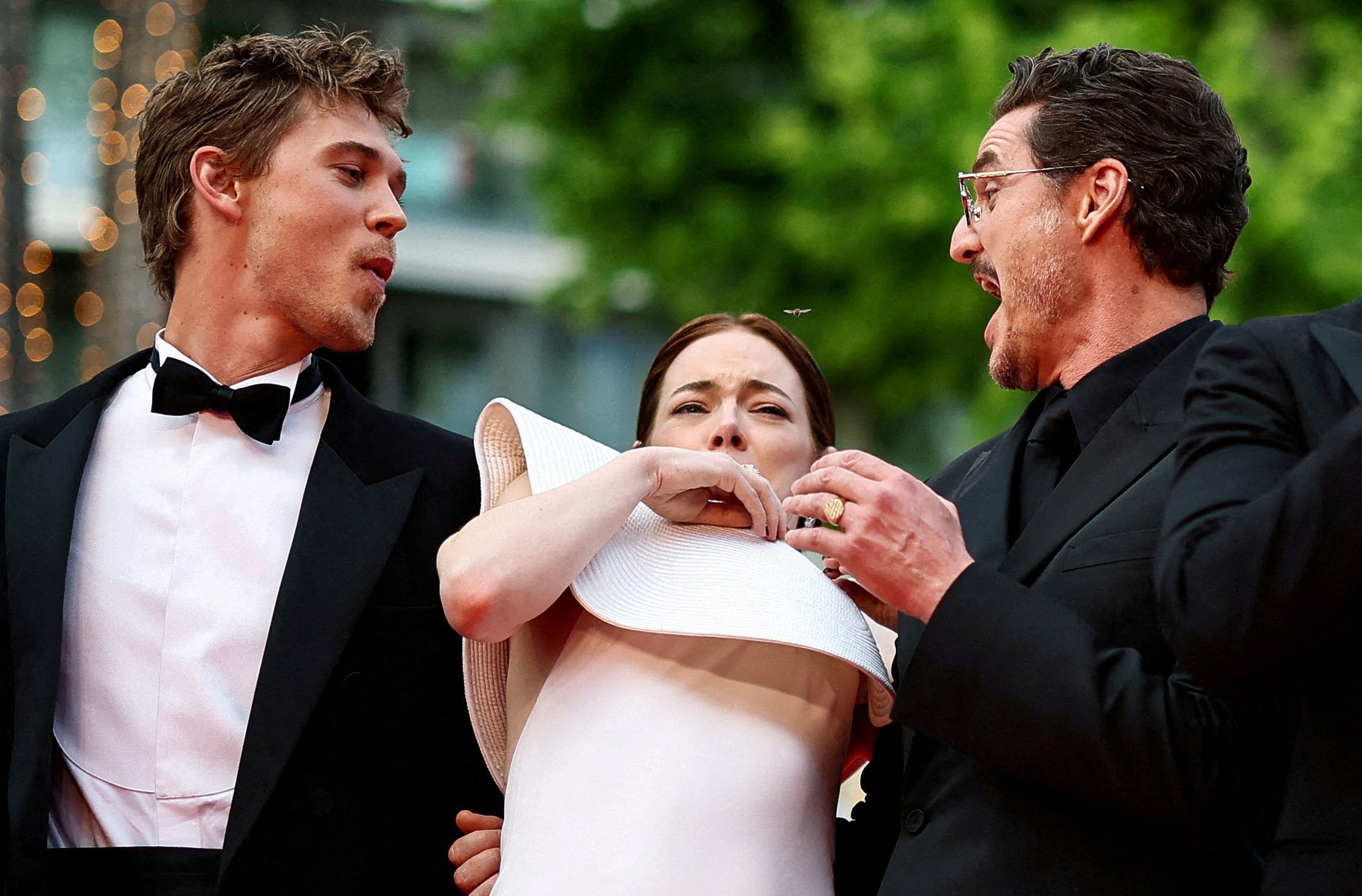 Austin Butler, Emma Stone, and Pedro Pascal react to a bee as they pose on a red carpet.