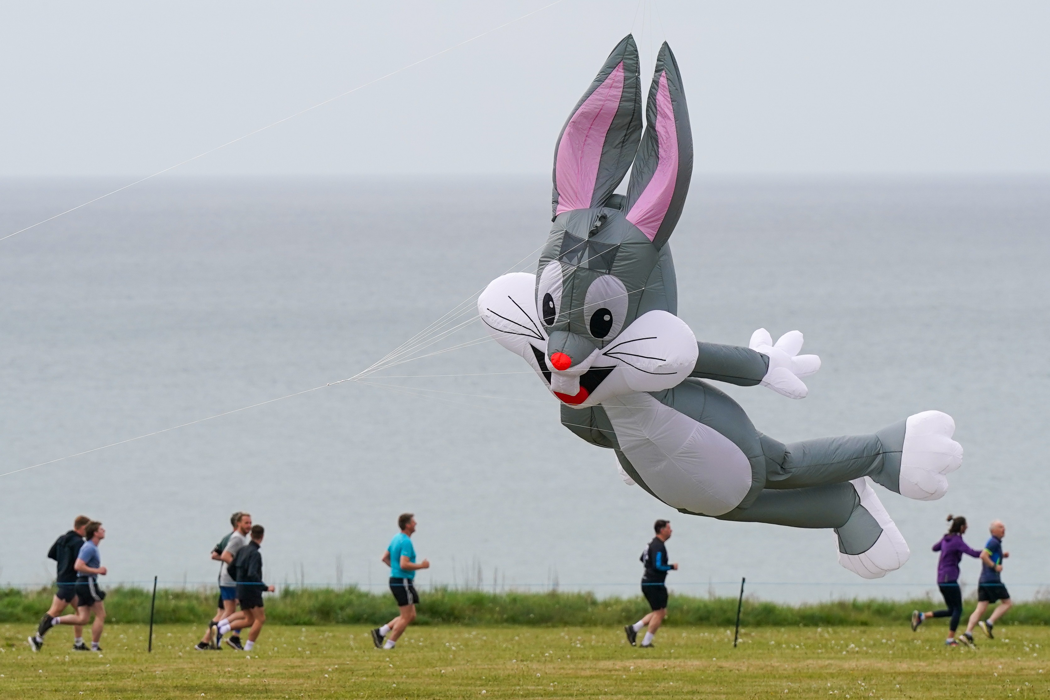 People run on a path beneath a large kite shaped like Bugs Bunny.