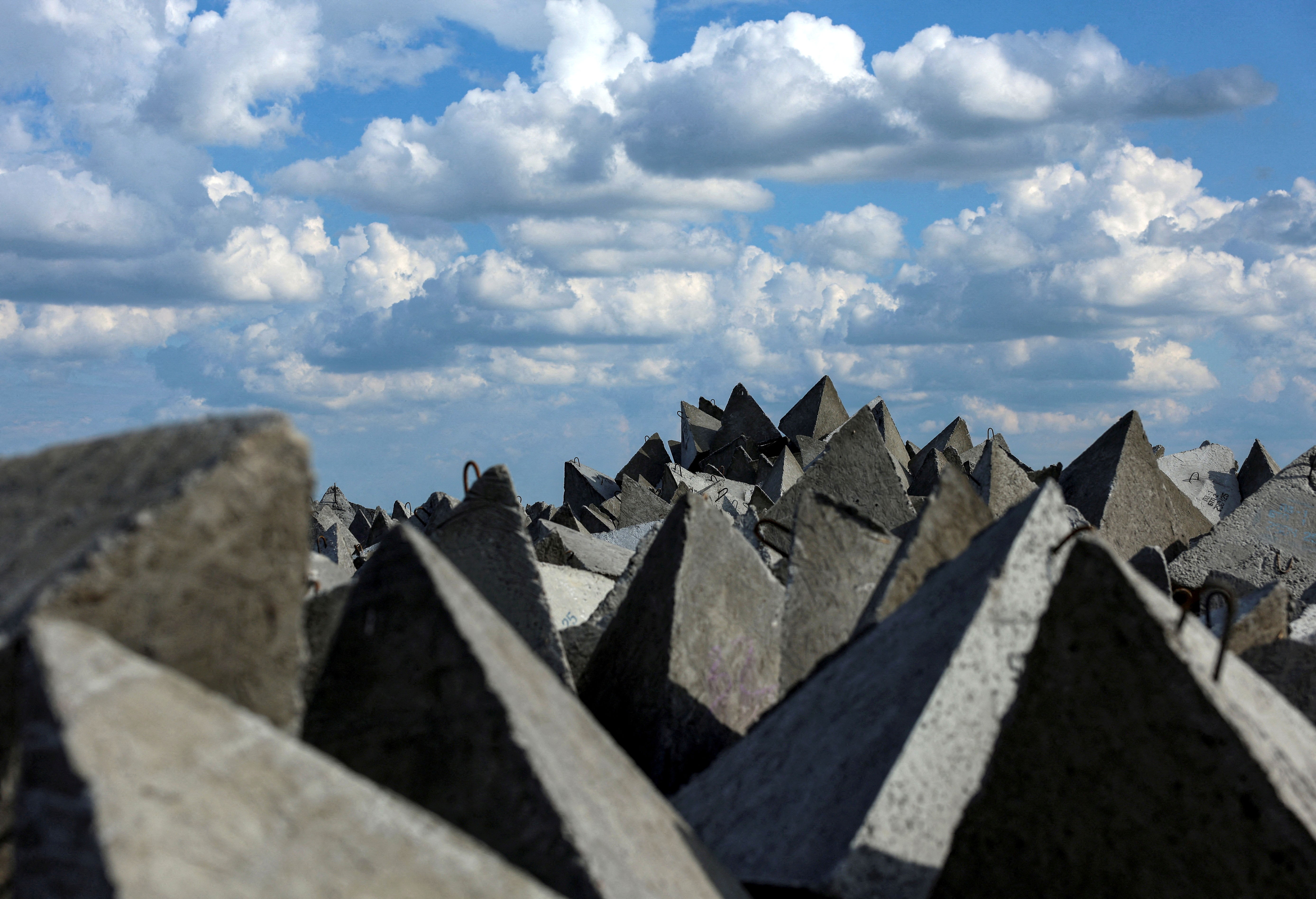 A pile of pyramid-shaped concrete anti-tank fortifications, seen beneath a cloudy sky