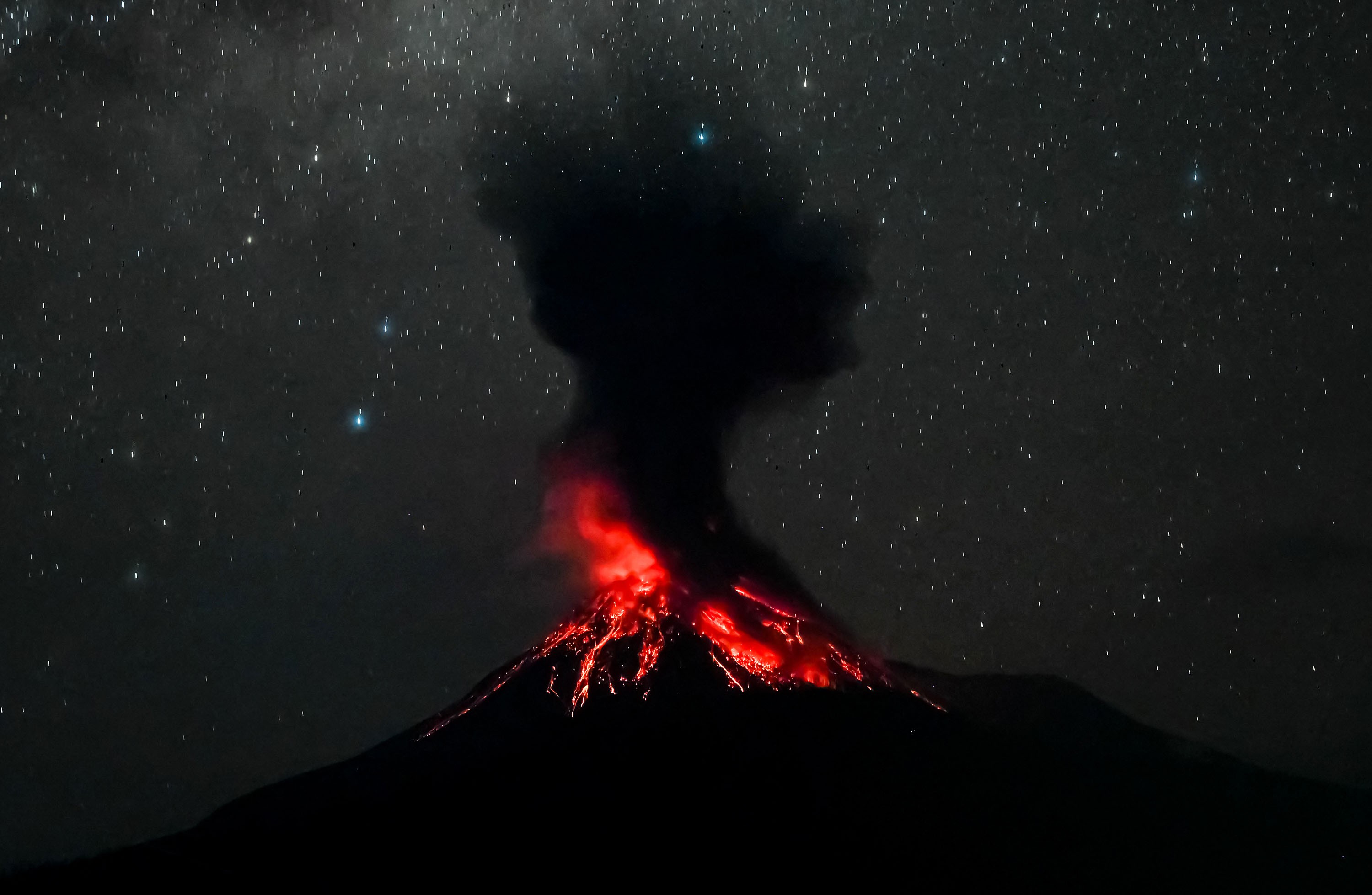 The top of an erupting volcano, seen at night beneath a starry sky.