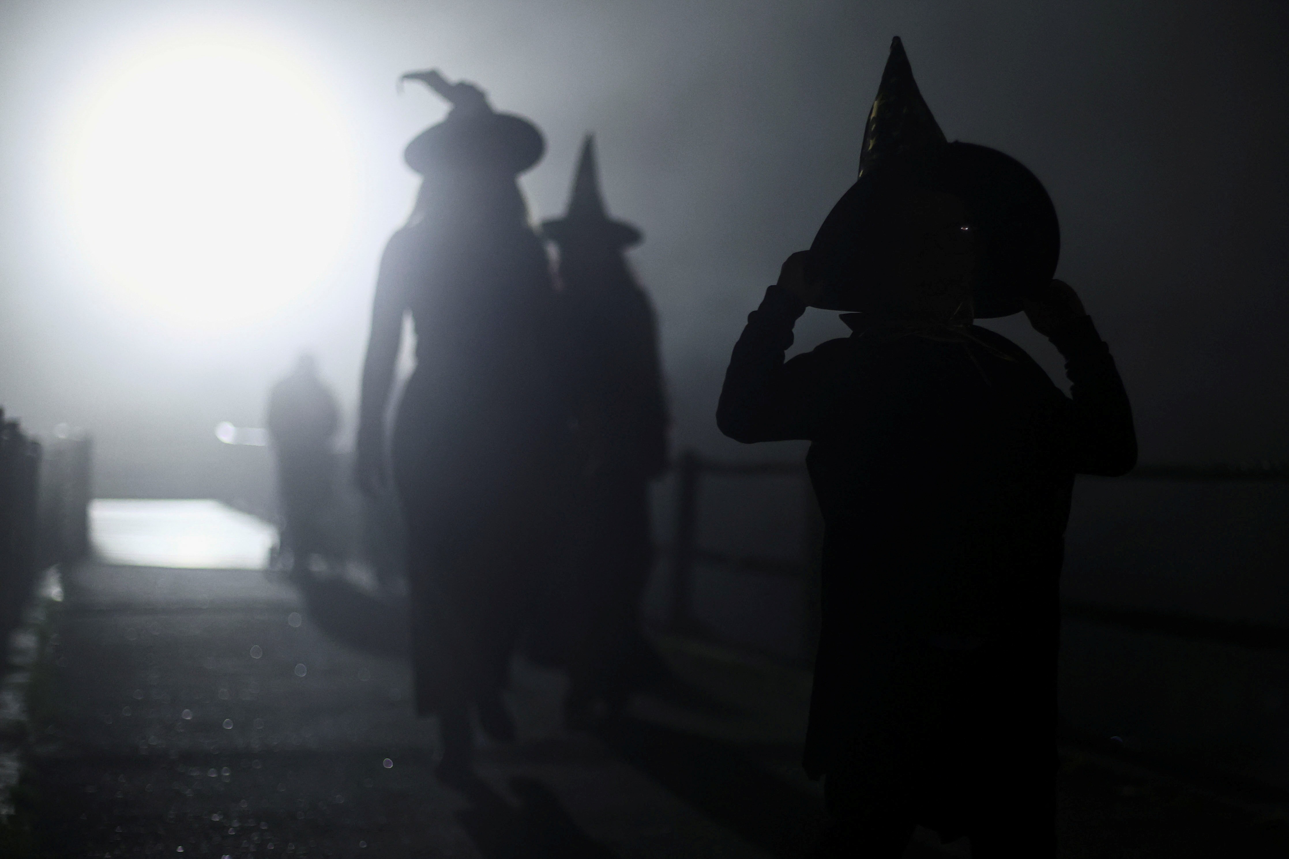Several people wearing witch costumes walk in a street at night.
