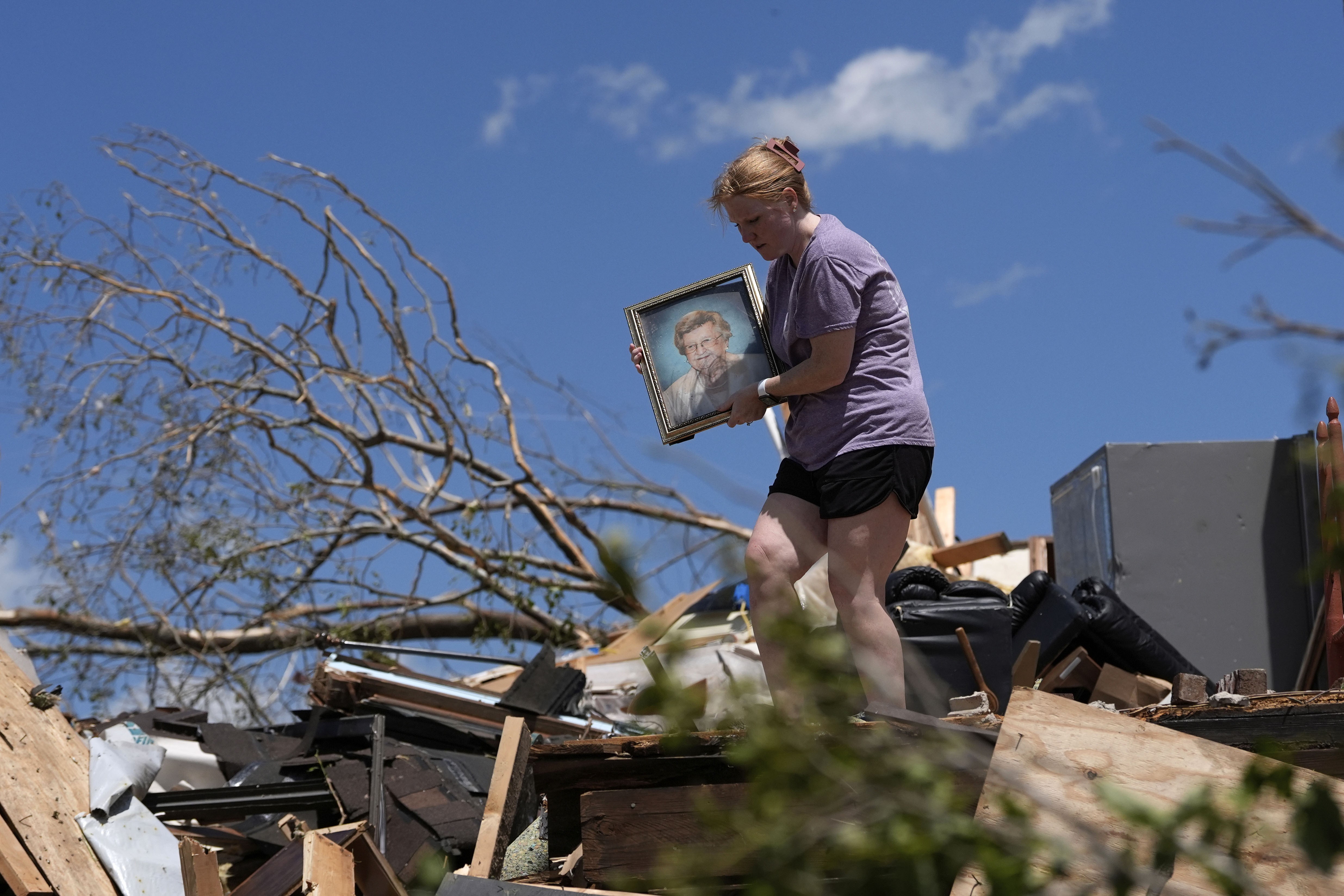 A person carries a family picture while walking over debris outside a storm-damaged house.