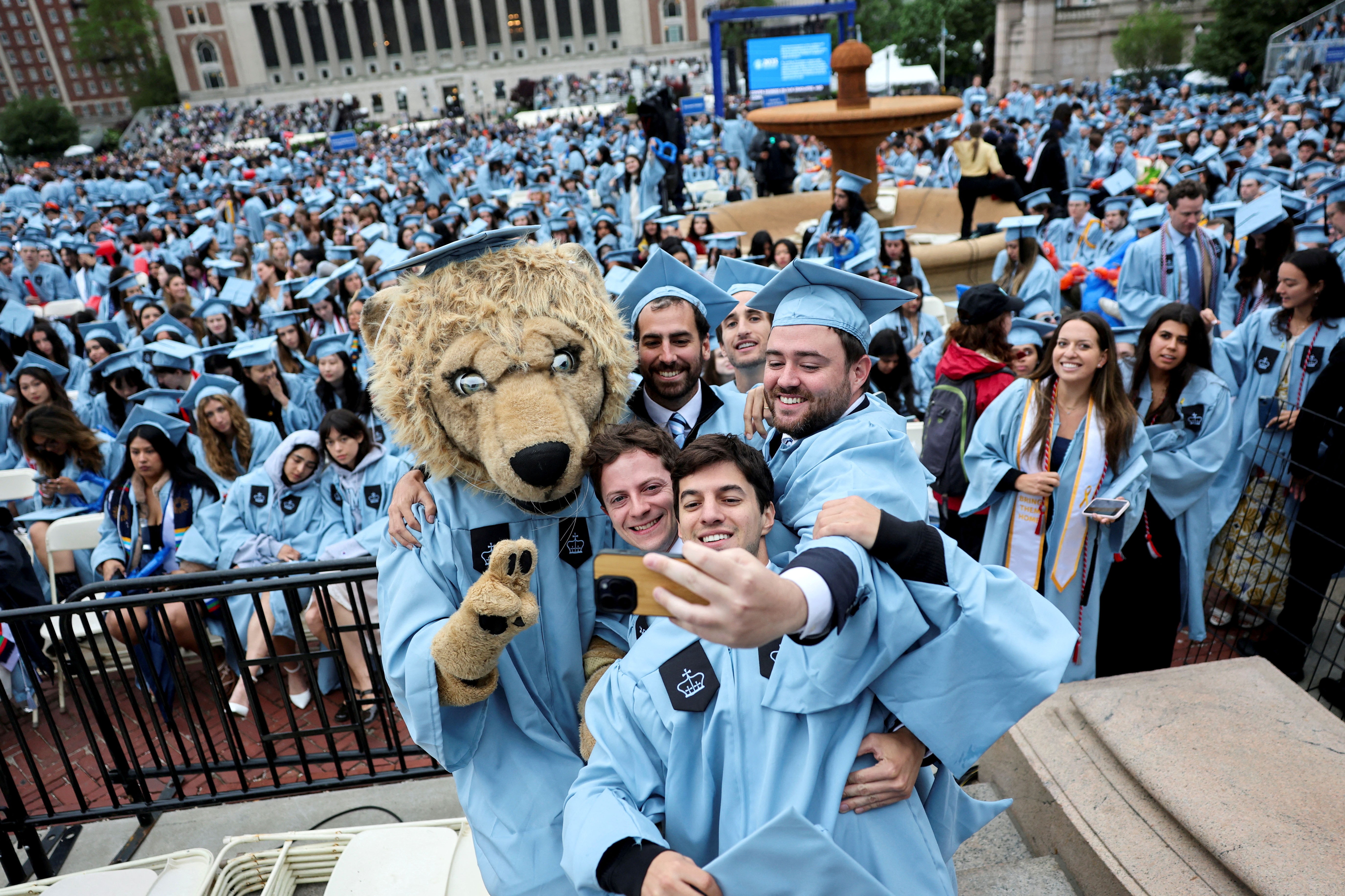 Graduating students pose with a person dressed as a lion mascot at a commencement ceremony.