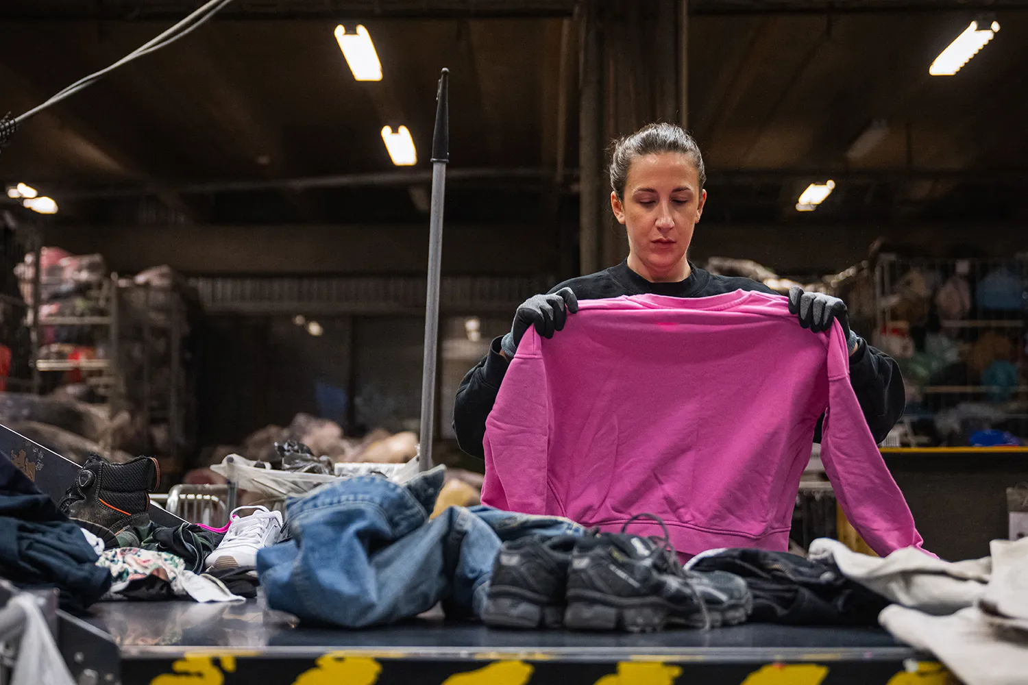 A worker holds up a pink sweatshirt at a clothing sorting center.