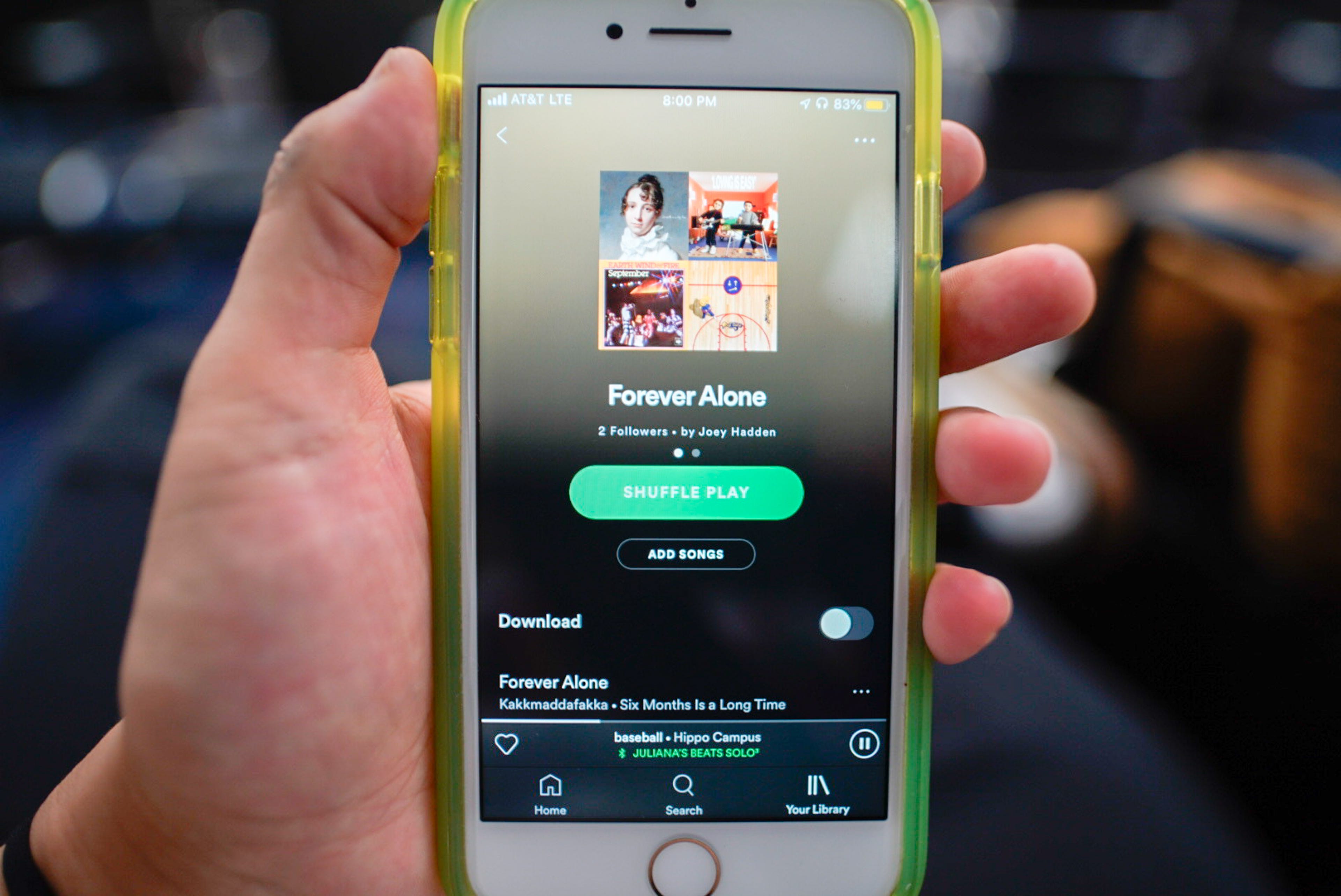 A hand holds a phone with a screen displaying a Spotify playlist