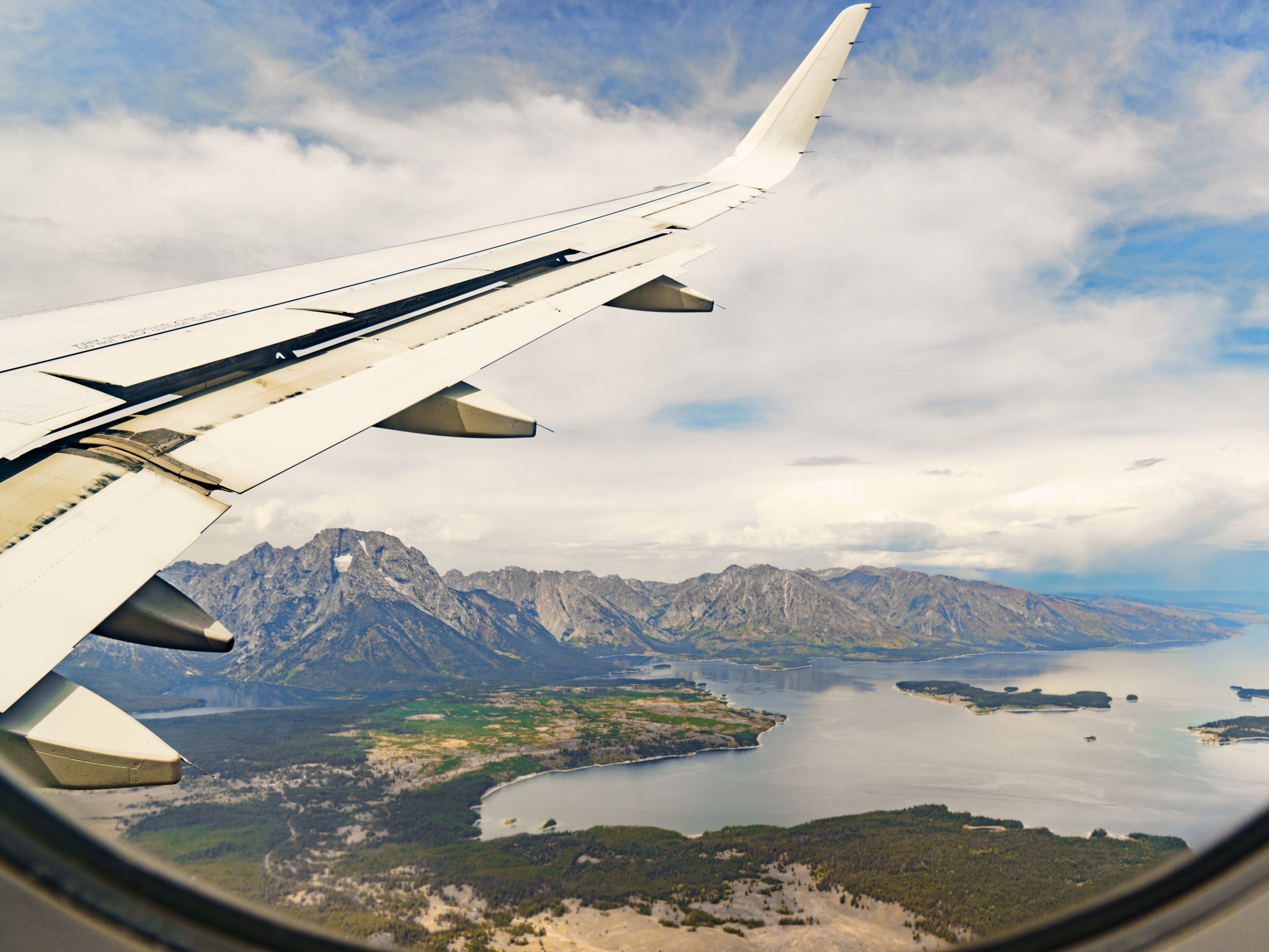 A view out a plane window with the wing on the left and mountains and lakes on the right.