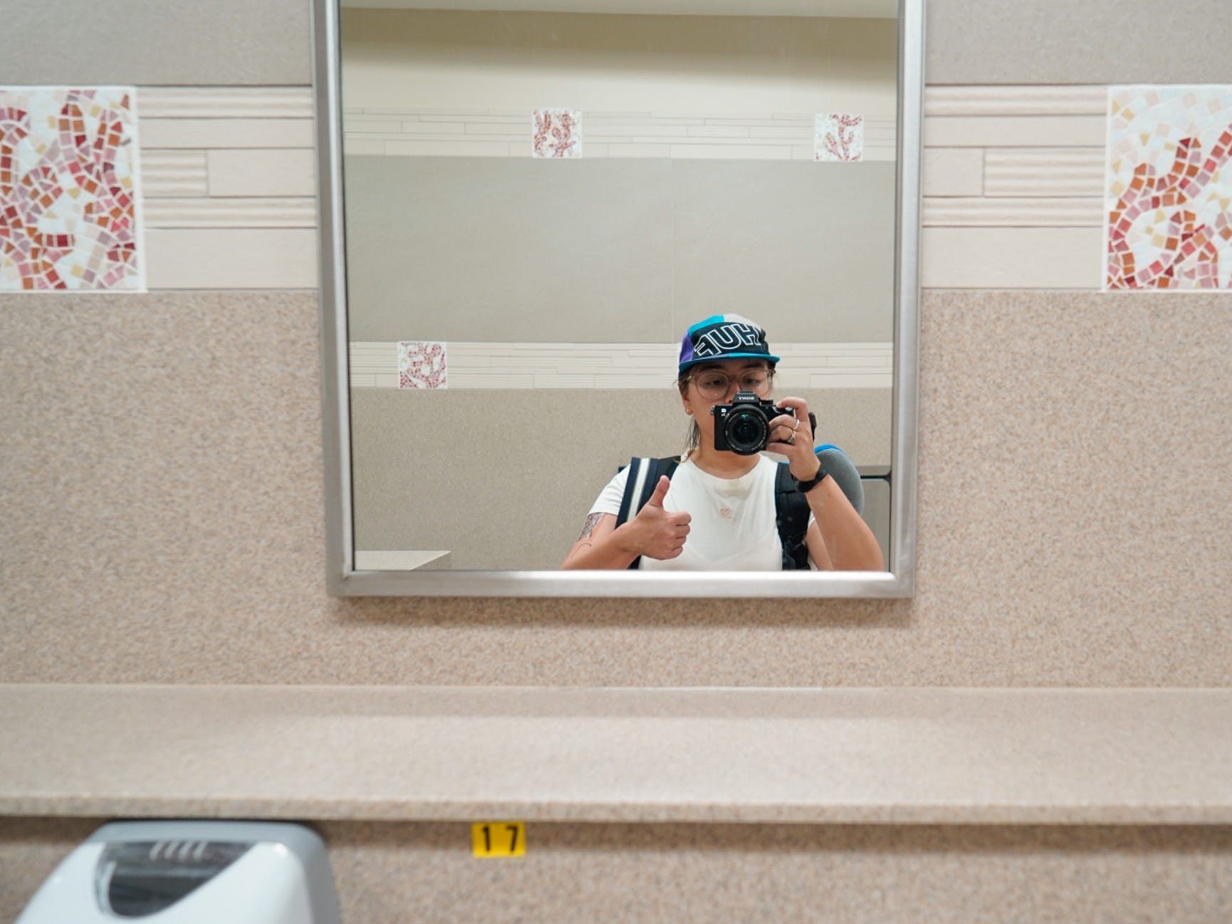 The author takes a mirror selfie with a thumbs up inside an airport bathroom