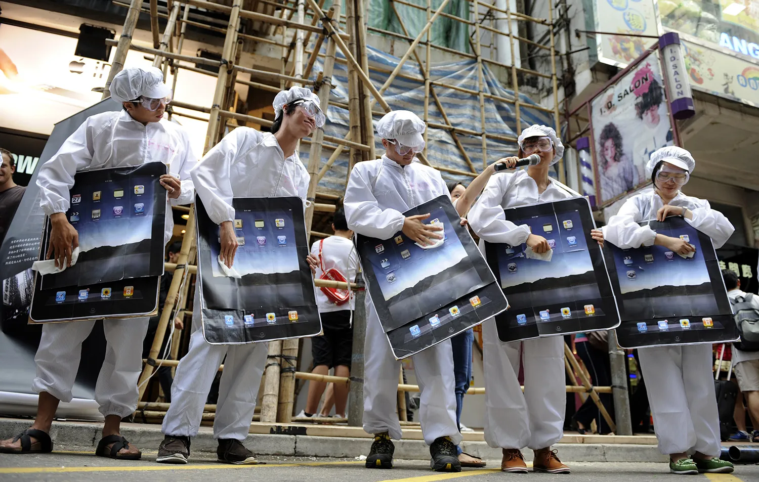 Protesters dressed in white gear as factory workers hold large fake iPads during a protest.