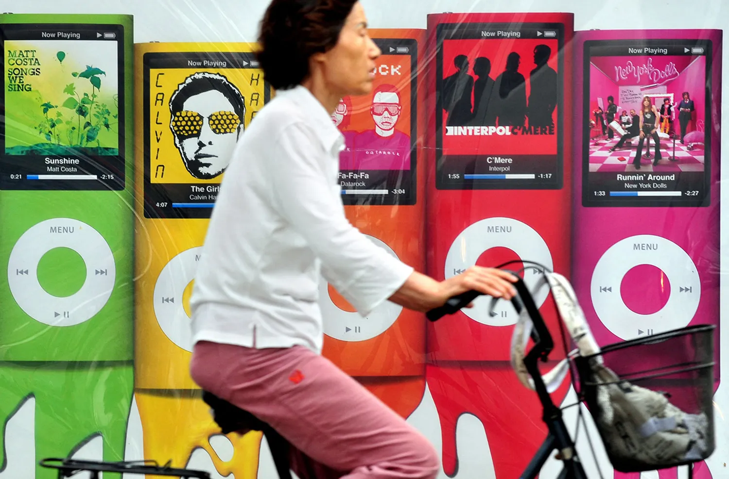 A person a bicycle rides pass a billboard displaying colorful iPod devices.