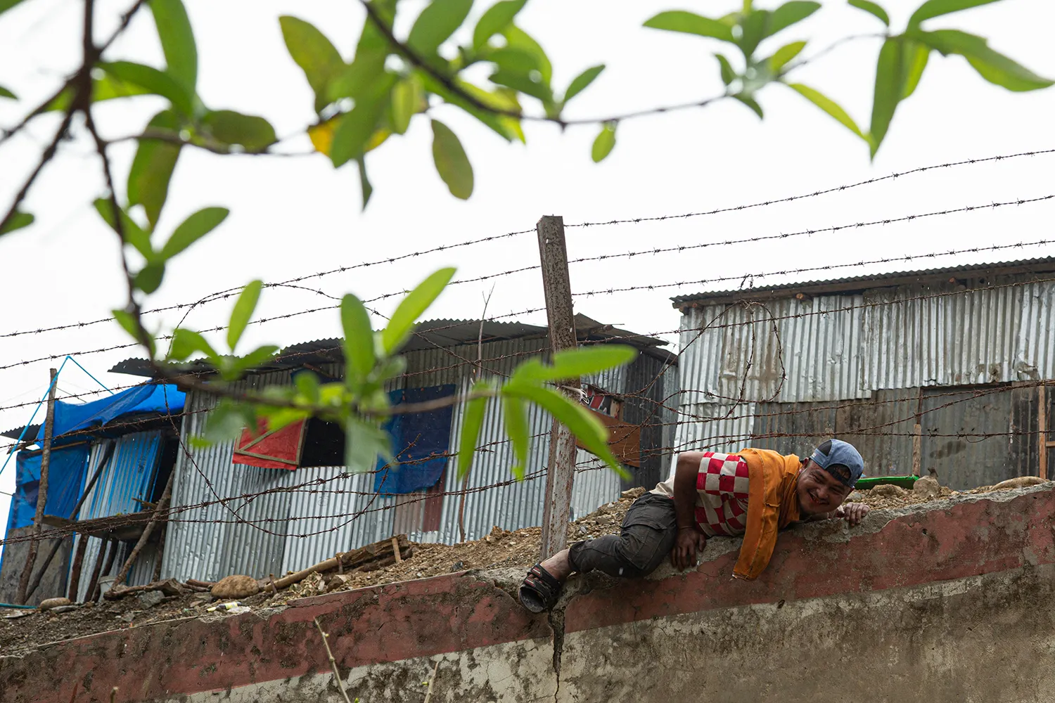 A Burmese refugee attempts to climb under a barbed wire fence.