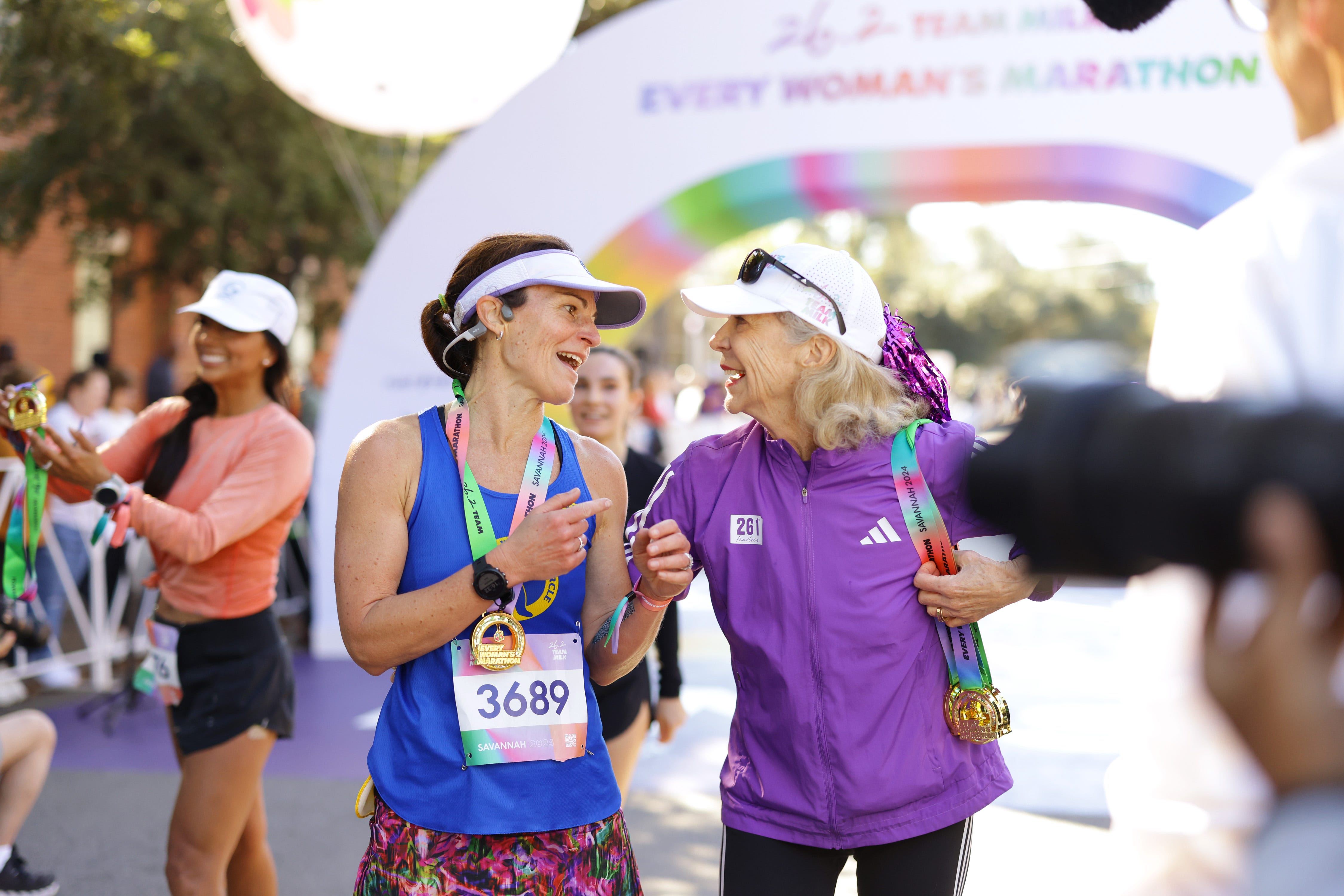 Two women, wearing medals and colorful clothes, chat at the finish line for Every Woman's Marathon.