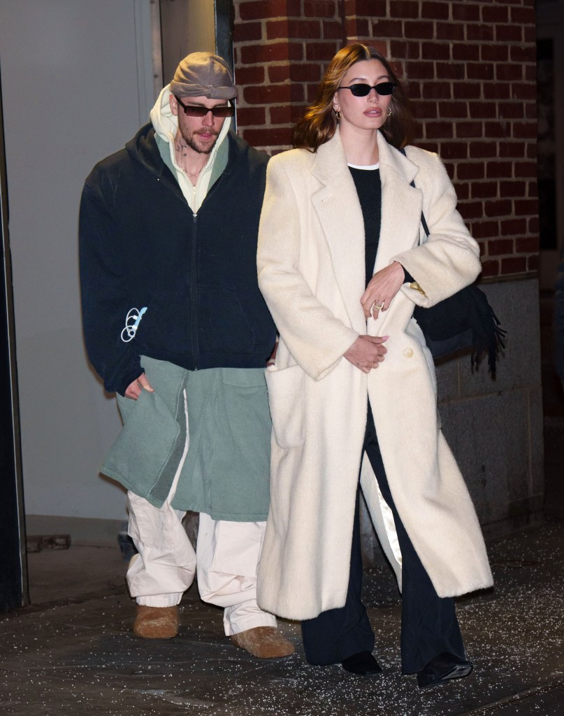Justin Bieber in over-sized clothing with Hailey Bieber in a jacket. Both are wearing sunglasses looking stern.