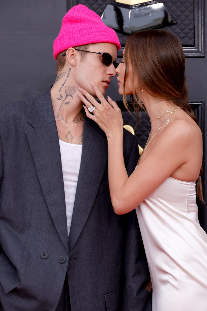 Justin Bieber wearing a pink hat kissing Hailey Bieber in a white dress.