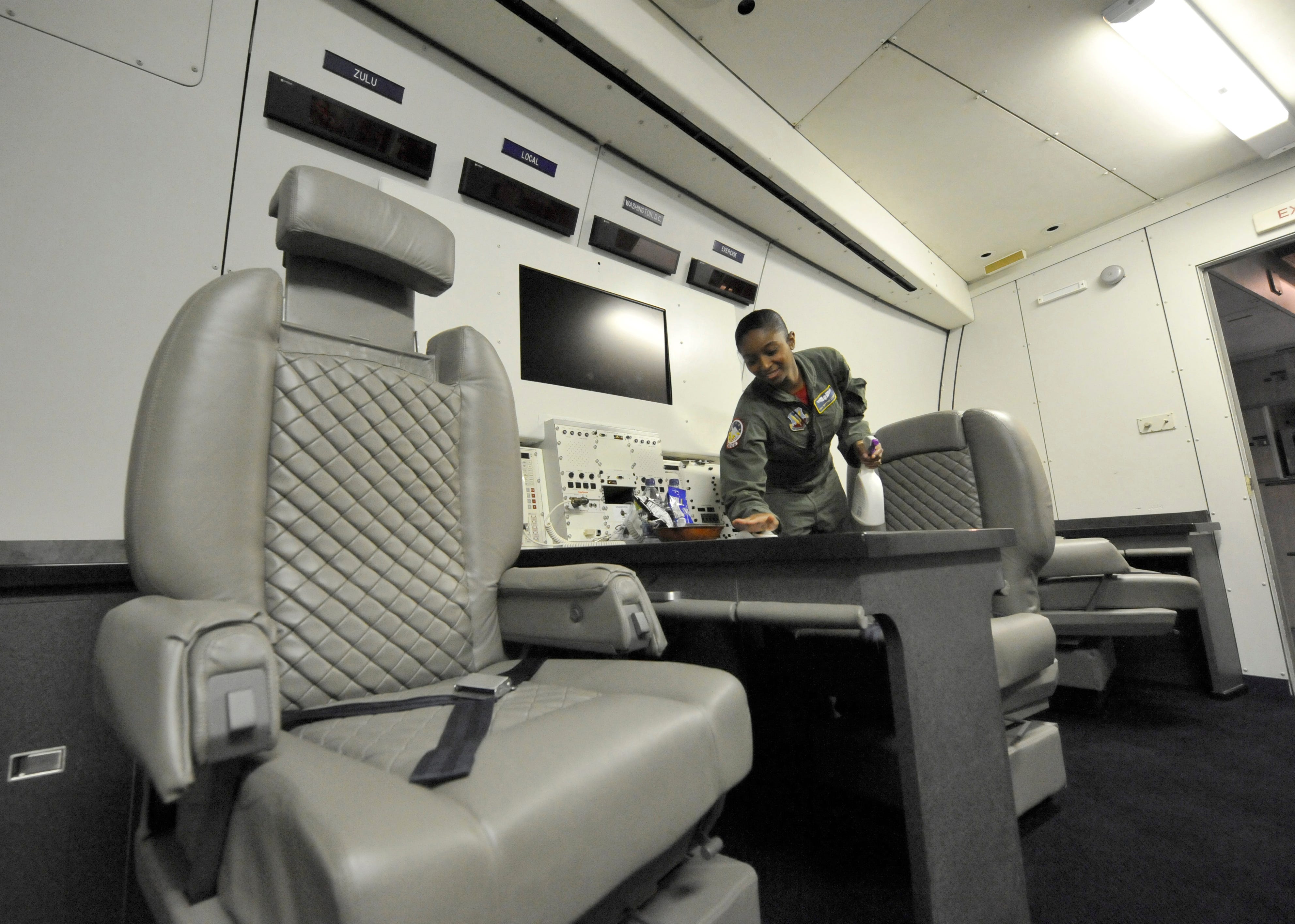 A flight attendant on an E-4B plane wipes down a table.
