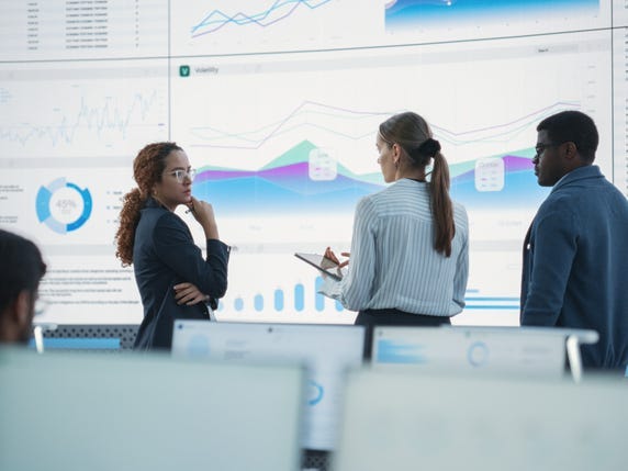 Businessmen and women standing in front of a data visualization board in a conference room