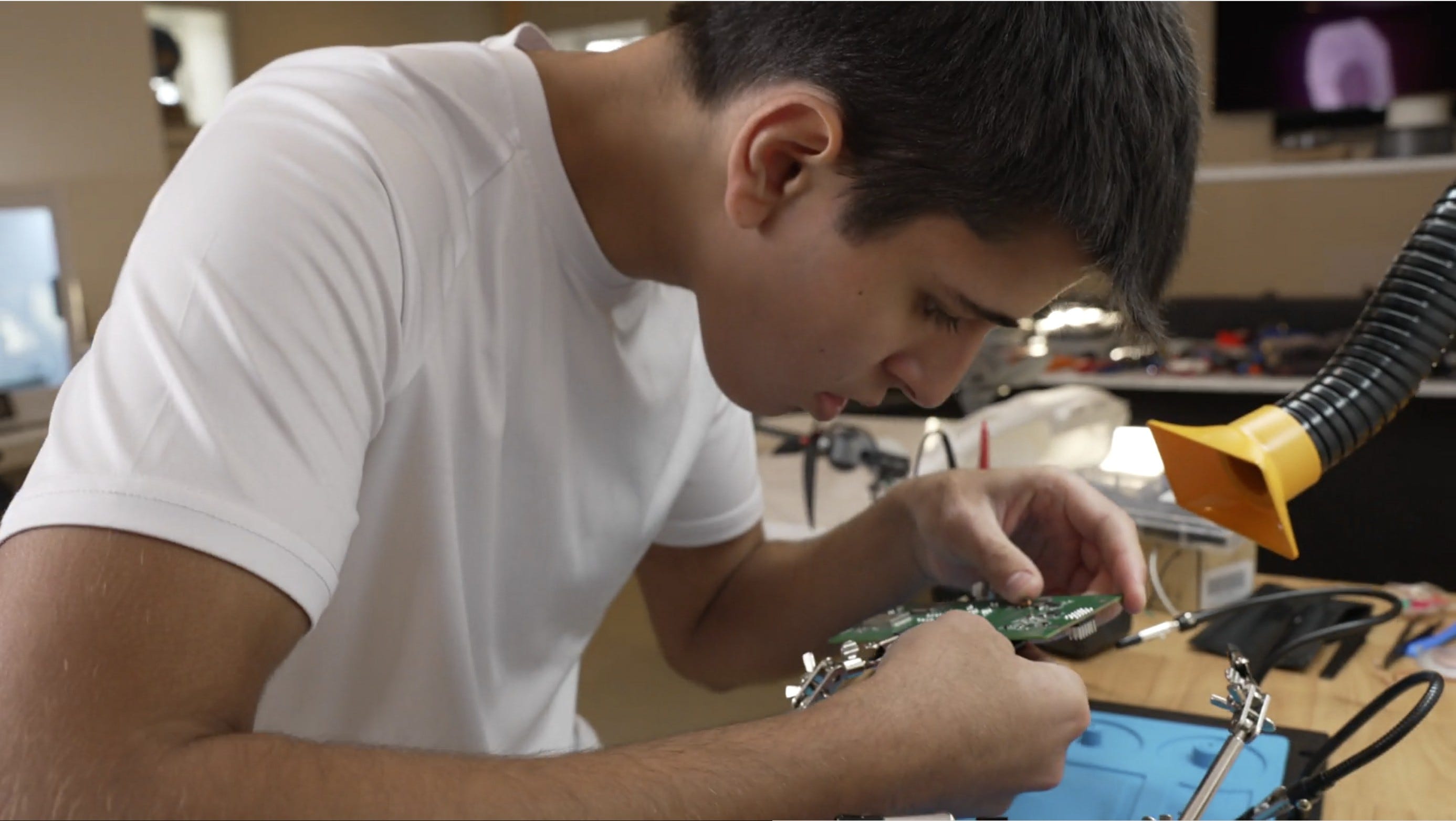 young man cooper taylor in white shirt bent over a small circuit board mounted on a desk