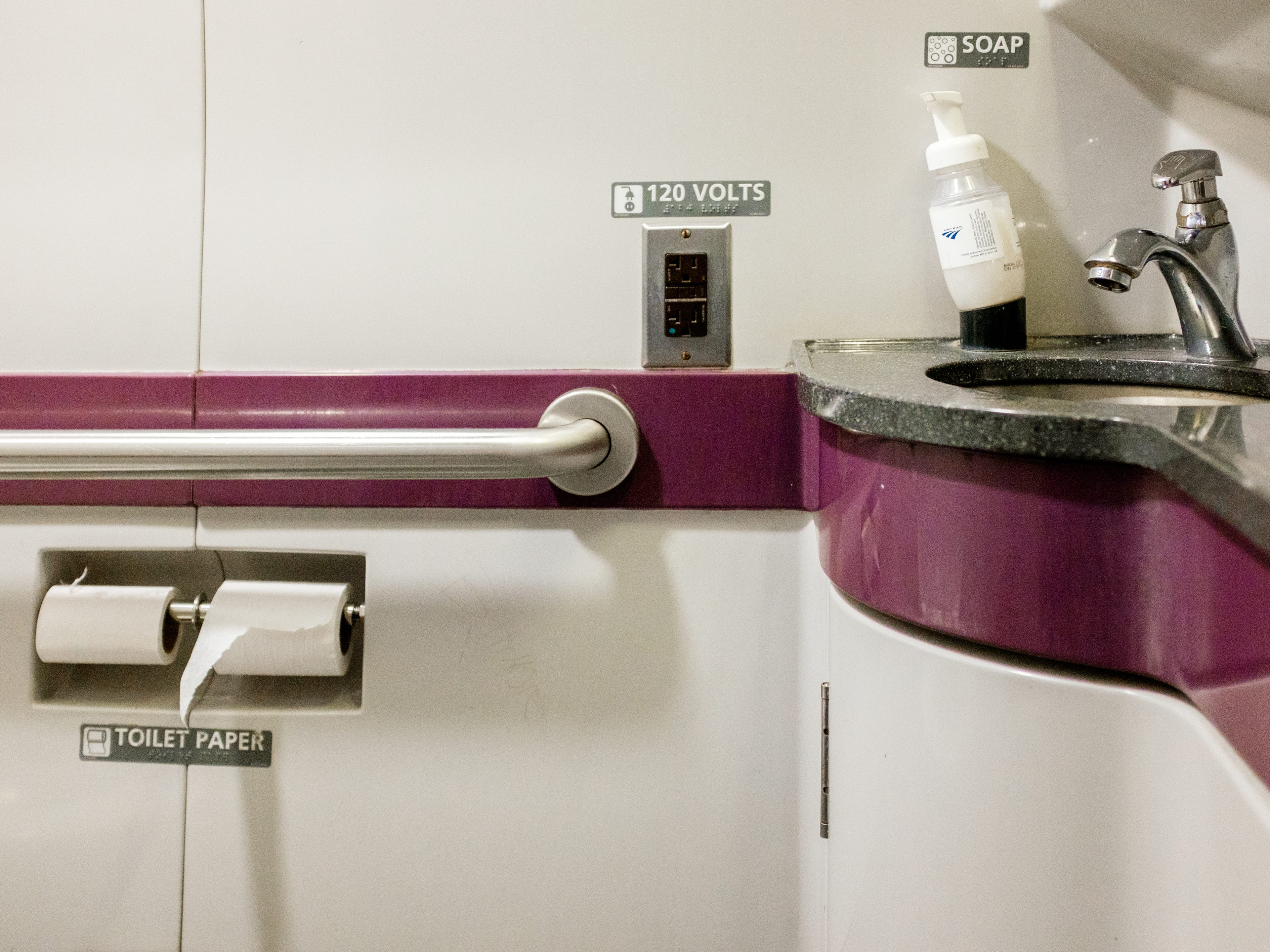 Inside a train bathroom with purple accents and a rink on the right