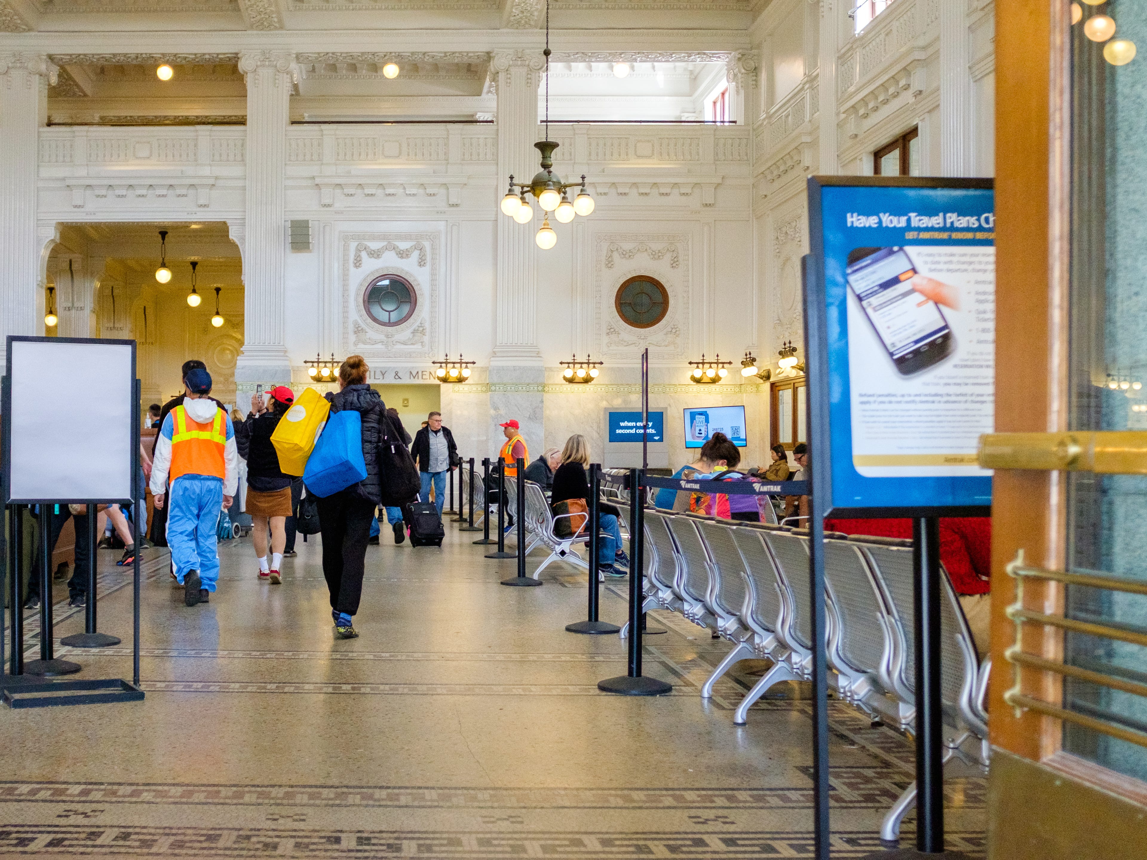 Travelers inside a train station with white, intricately molded walls and high ceilings