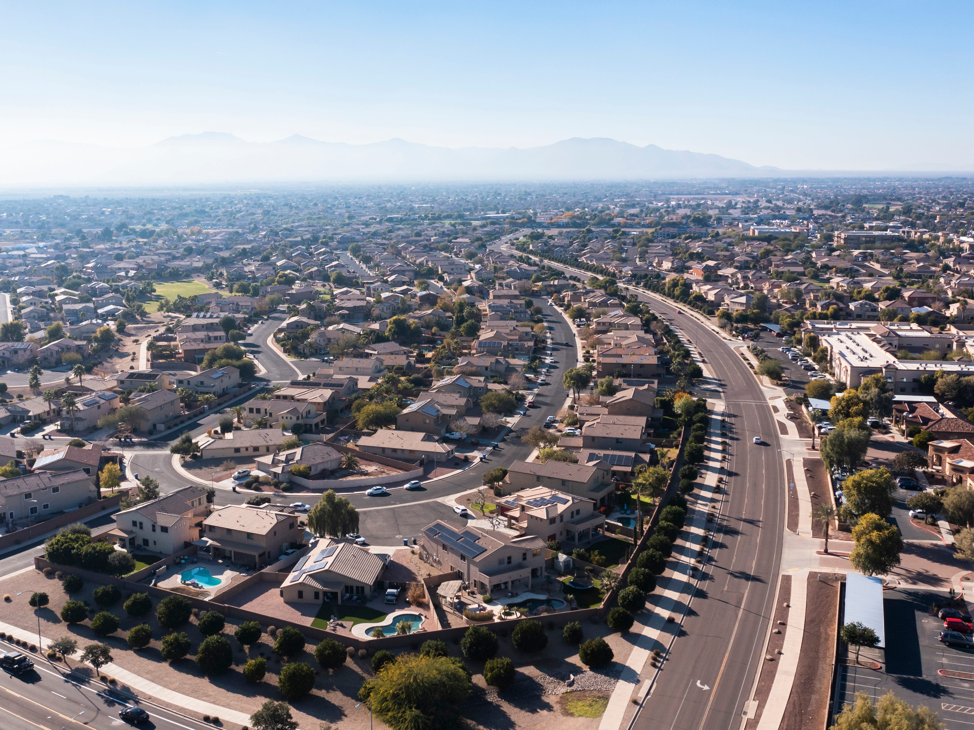 Many homes neatly layed out near a winding roads with mountains in the background
