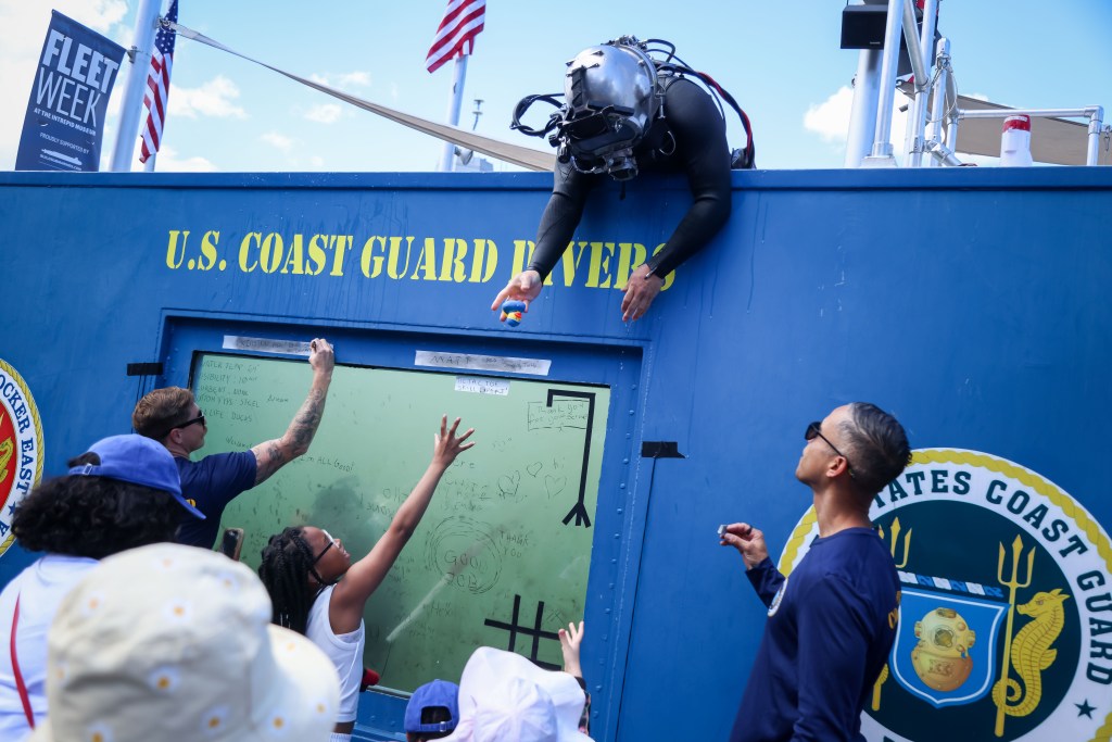 U.S. Coast Guard Divers hand rubber ducks out to children from a dive tank.