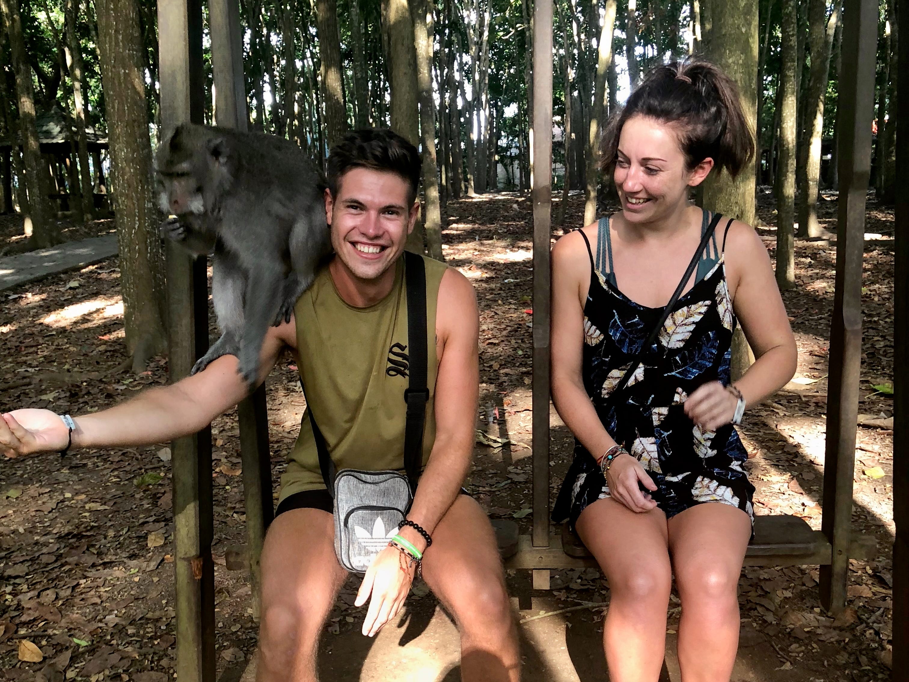 A couple posing with a monkey in a forest.