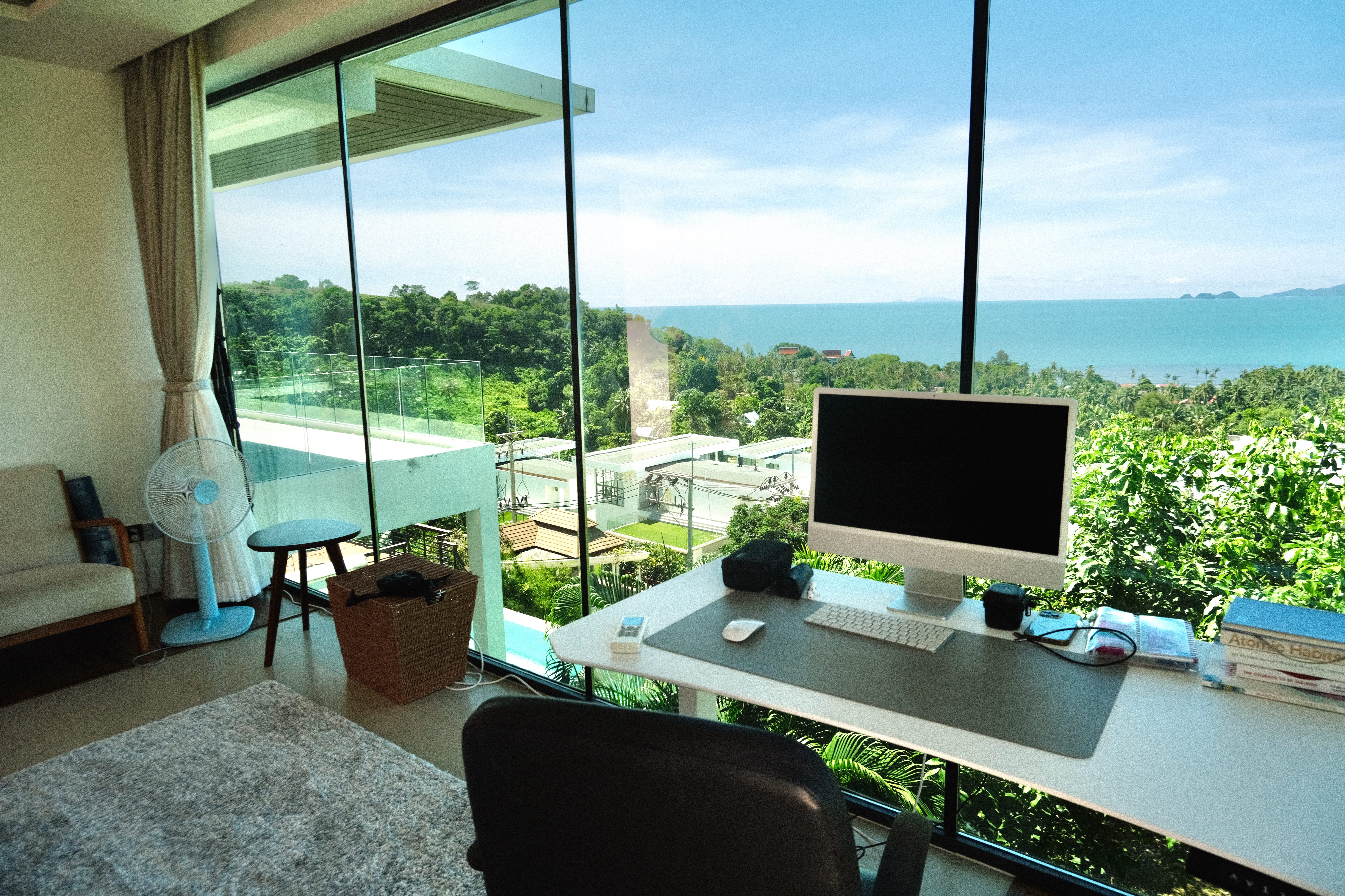 A computer desk facing a window that overlooks the lush hills and sea in Koh Samui, Thailand.