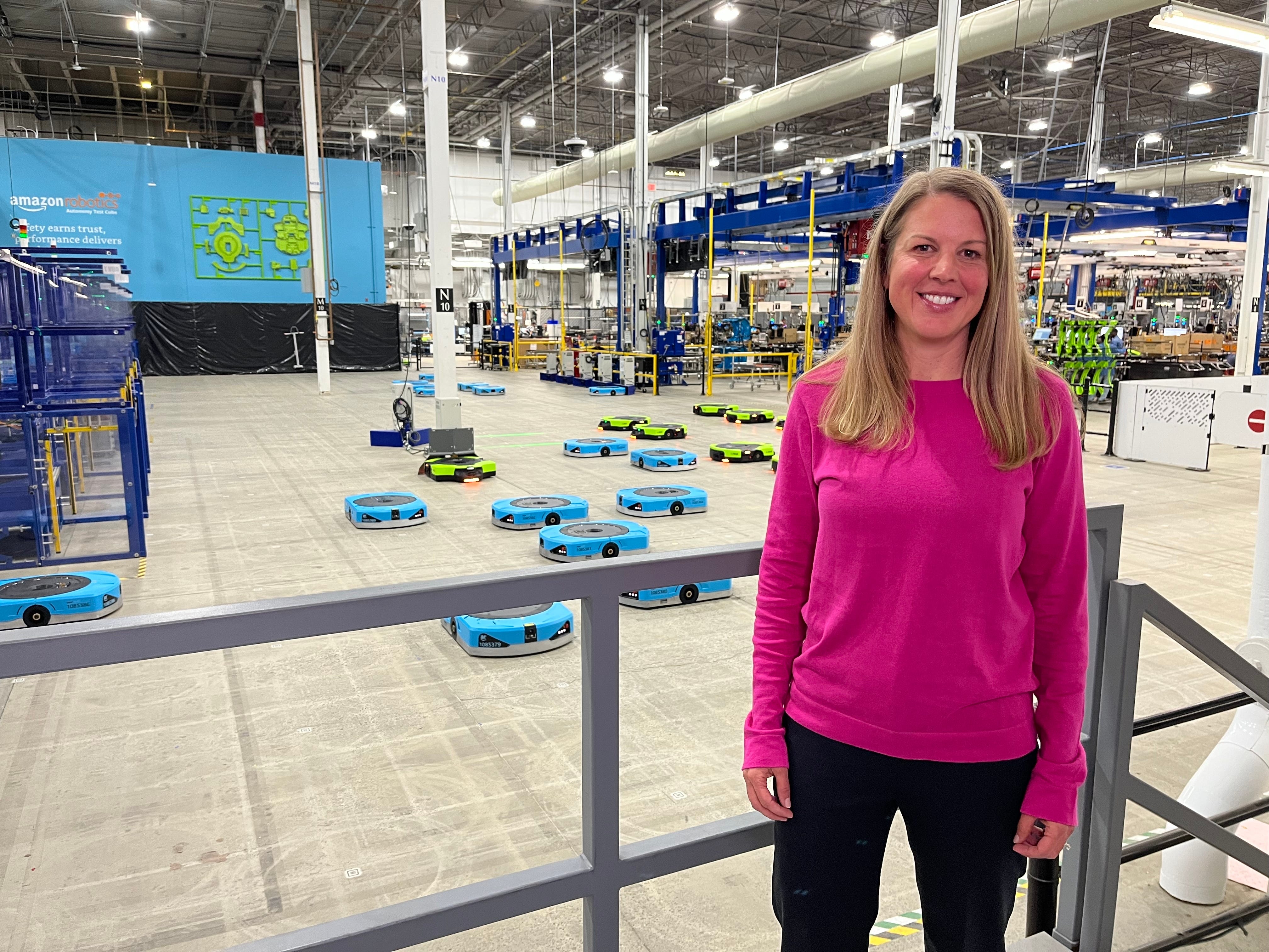 Erica McClosky leads manufacturing for Amazon Robotics and is pictured wearing a pink sweater in front of Amazon's blue and green robots