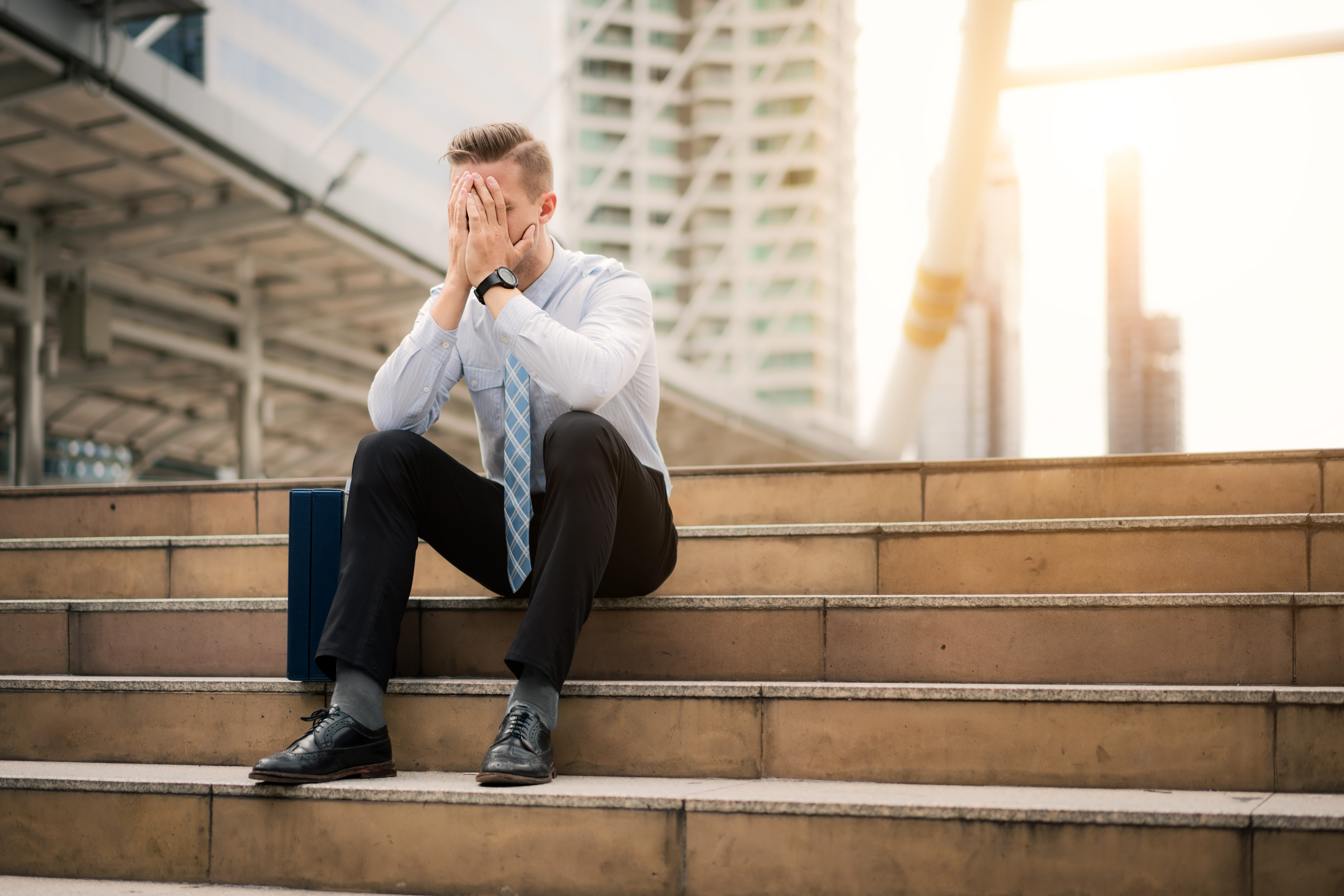 A man in a suit on steps, with his head in his hands.