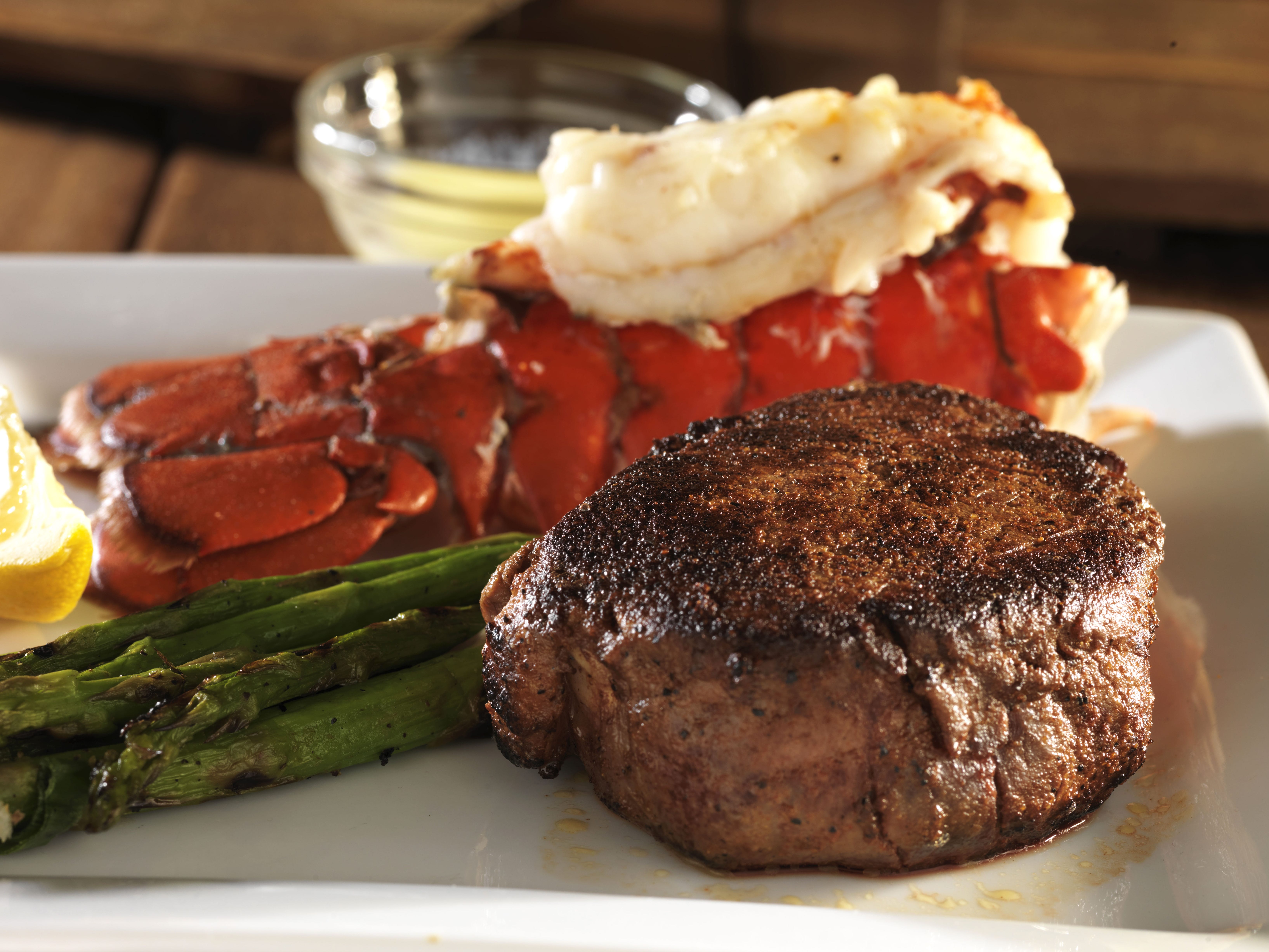 Steak, lobster, and asparagus on a plate with a side of drawn butter.