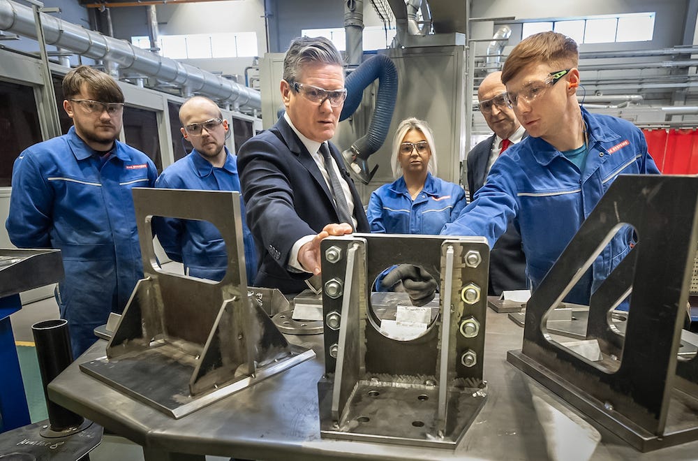 Sir Keir Starmer looks at metal parts and speaks to workers at BAE Systems in Barrow-in-Furness, UK, during a 2024 general election campaign stop.