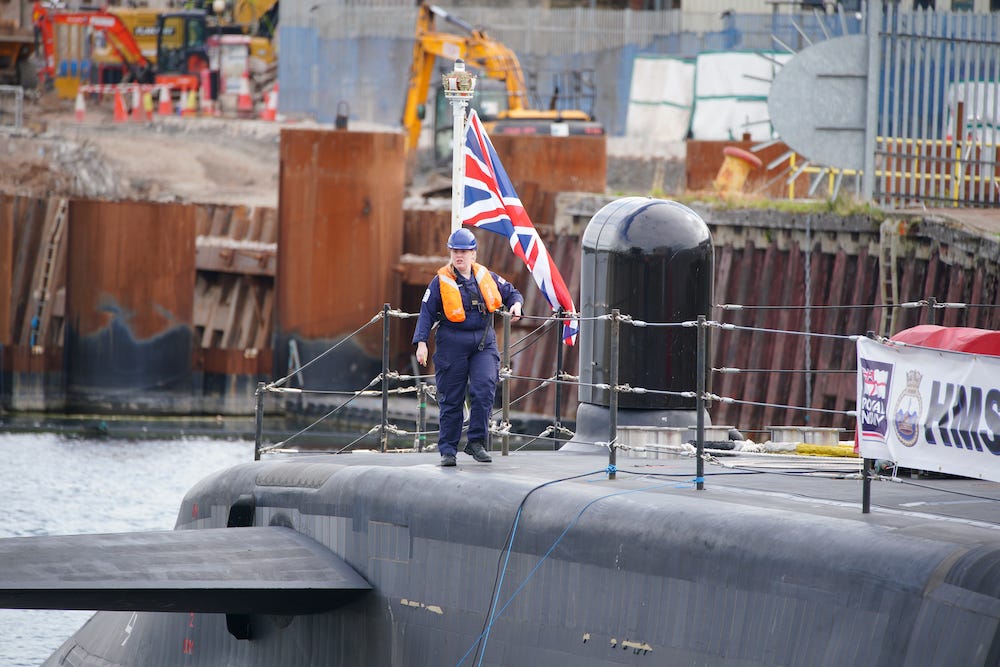 A worker walks across the deck of HMS Anson docked at BAE systems in Barrow-in-Furness before it is officially commissioned into the Royal Navy in 2022, with a British flag in the background