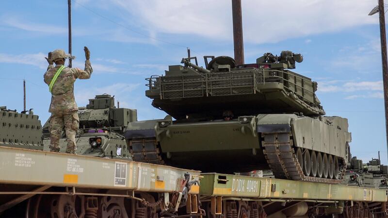 A soldier directs a green pained M1A1 Abrams tank on to a rail transporter