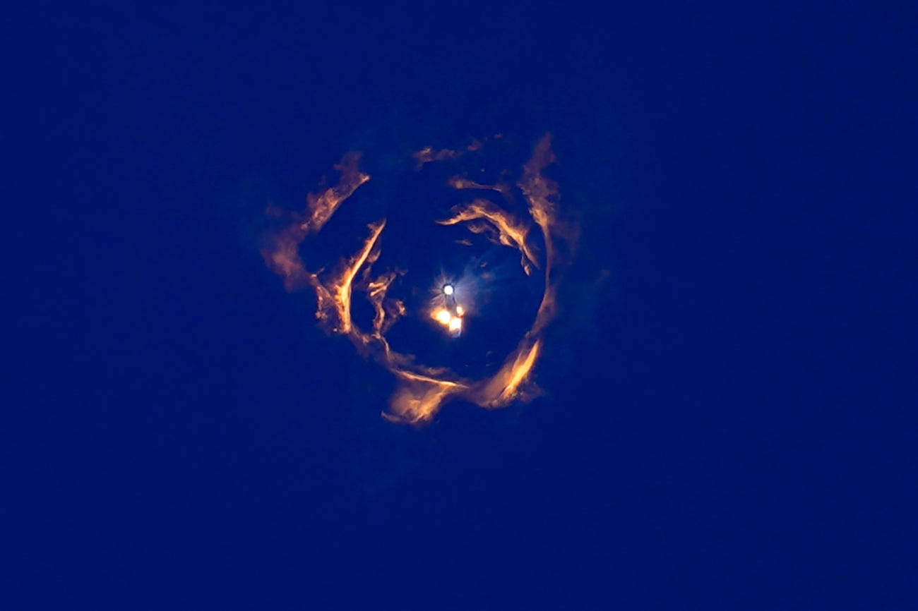 concentric circles of fire surround the faint silhouette of a starship rocket with bright lights against a dark blue sky
