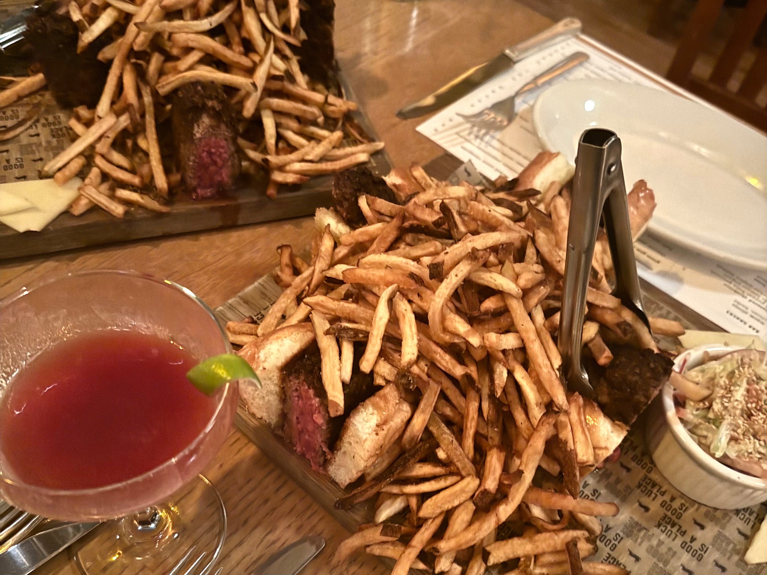 Two large plates of burgers and fries with a cocktail in the bottom left corner of the frame.