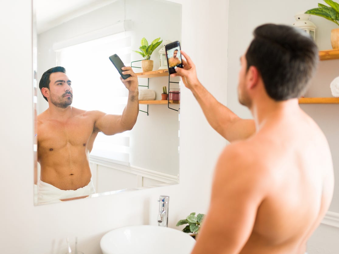 A shirtless man taking a mirror selfie.