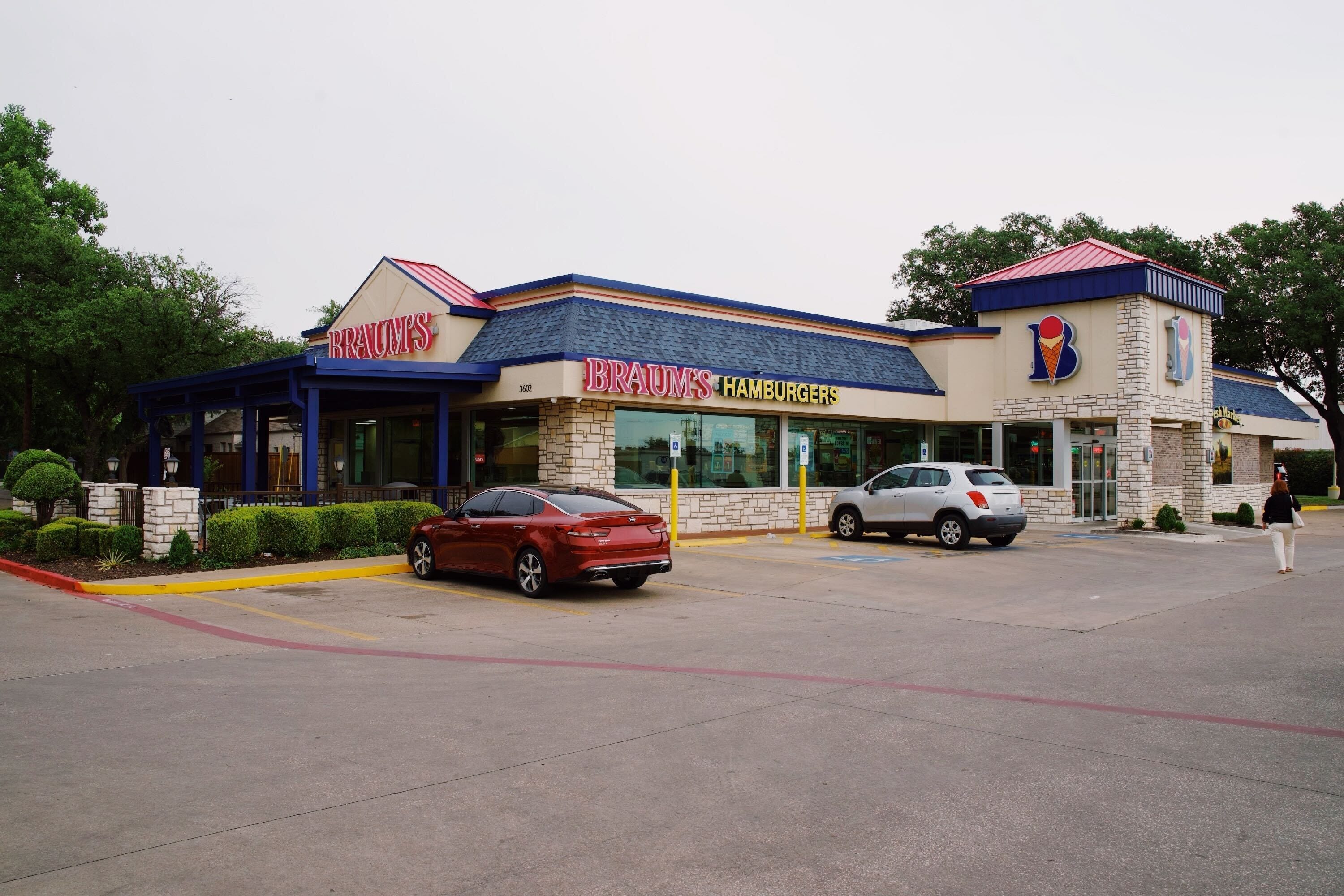 The exterior of a Braum's building. Two cars sit in the parking lot and a woman is walking towards the store's entrance.