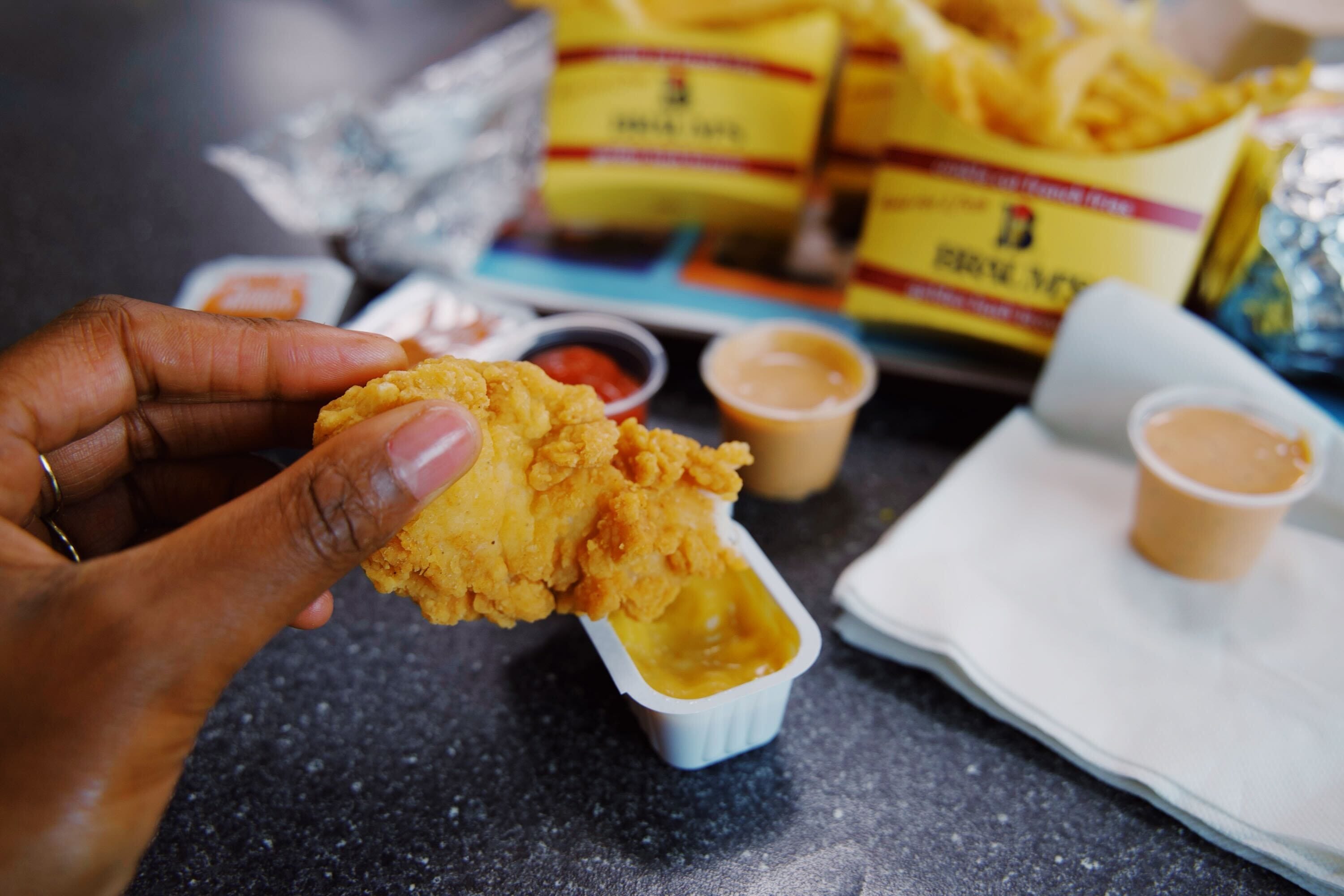 A hand dunking a chicken tender into honey mustard.