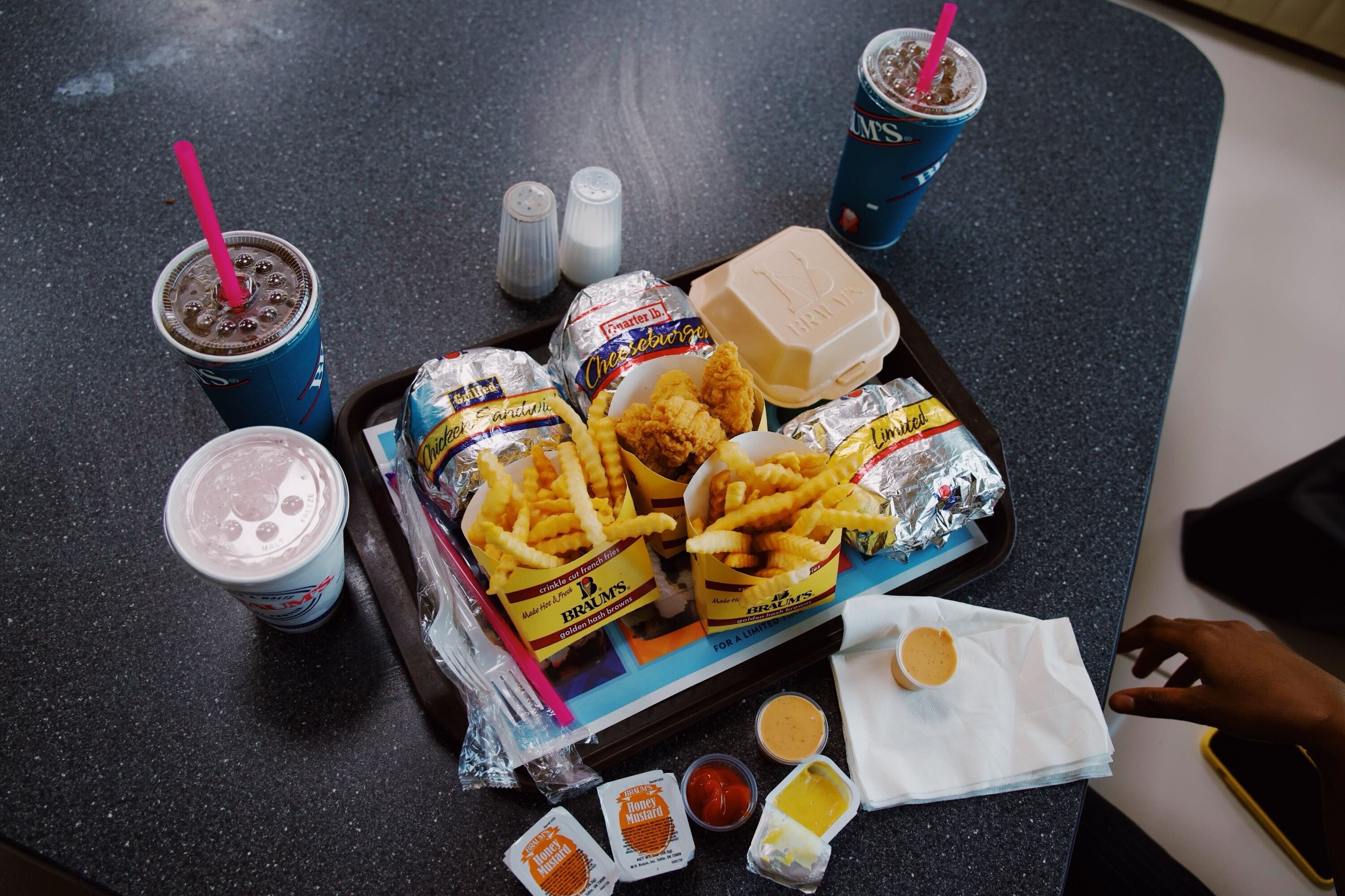 An overview of a trade full of food from the Braum's restaurant, including chicken tenders, 3 sandwiches, and 2 fry boxes.