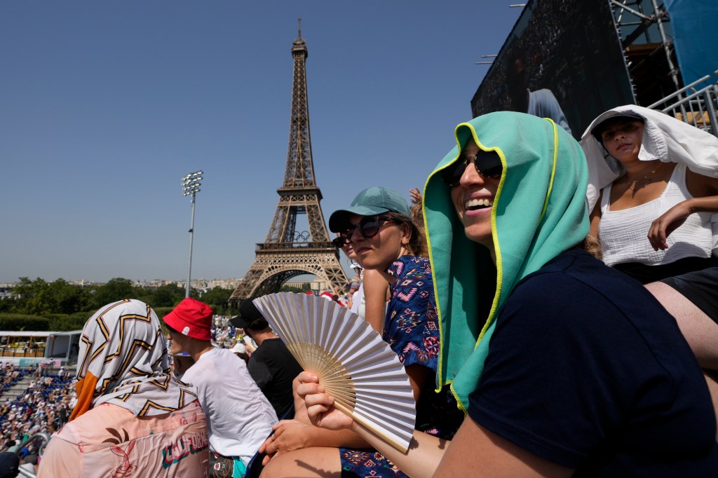 Stephanie Touissaint, foreground, uses a fan to keep cool in the sweltering heat at Eiffel Tower Stadium during a beach volleyball match between Cuba and Brazil at the 2024 Summer Olympics, July 30, 2024, in Paris, France.
