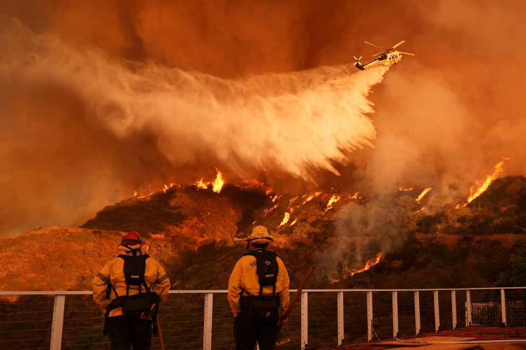 Firefighters watch a helicopter drop water on the Palisades Fire in Mandeville Canyon in Los Angeles, Jan. 11, 2025.