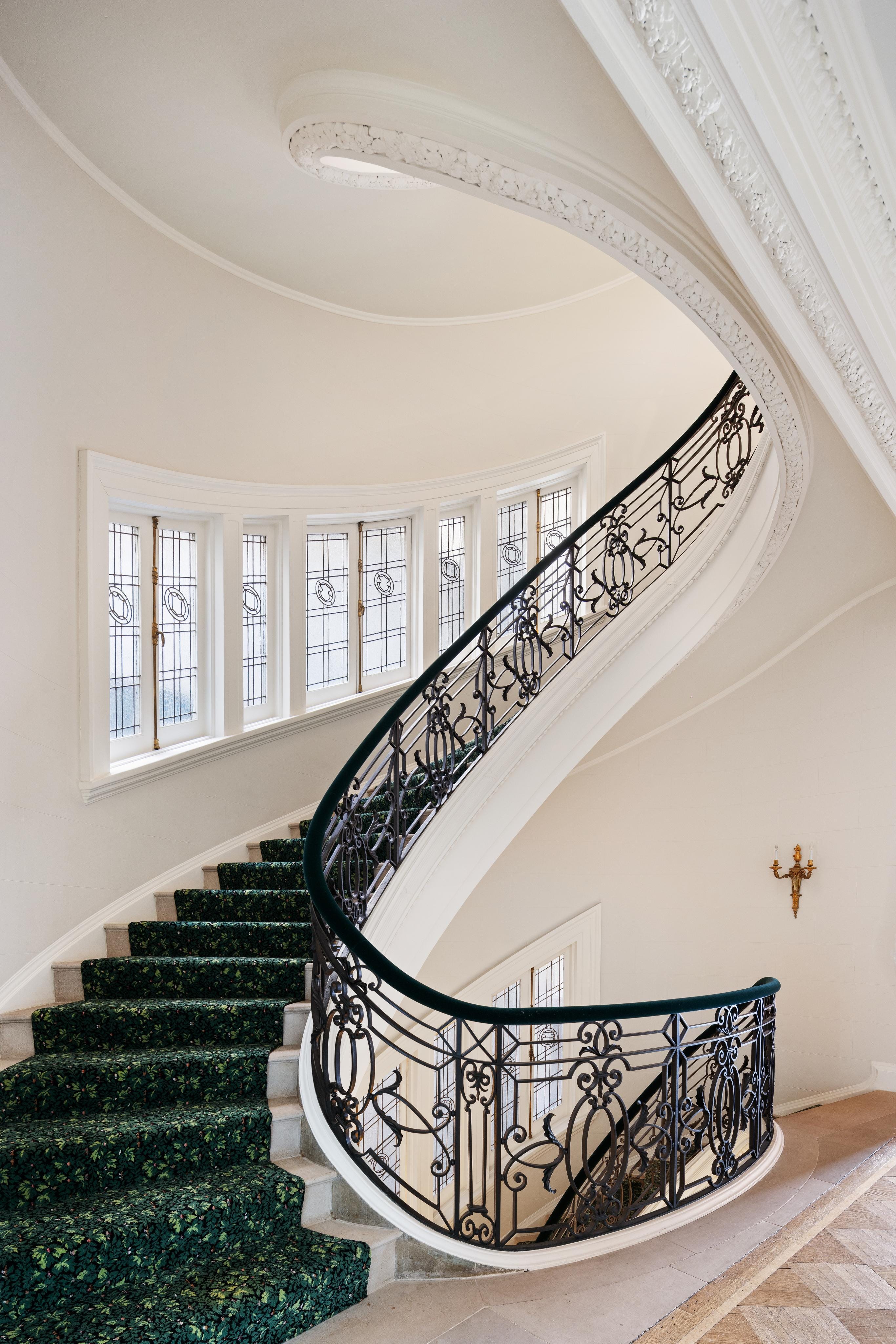 a limestone winding staircase with wrought iron railings and green carpeting