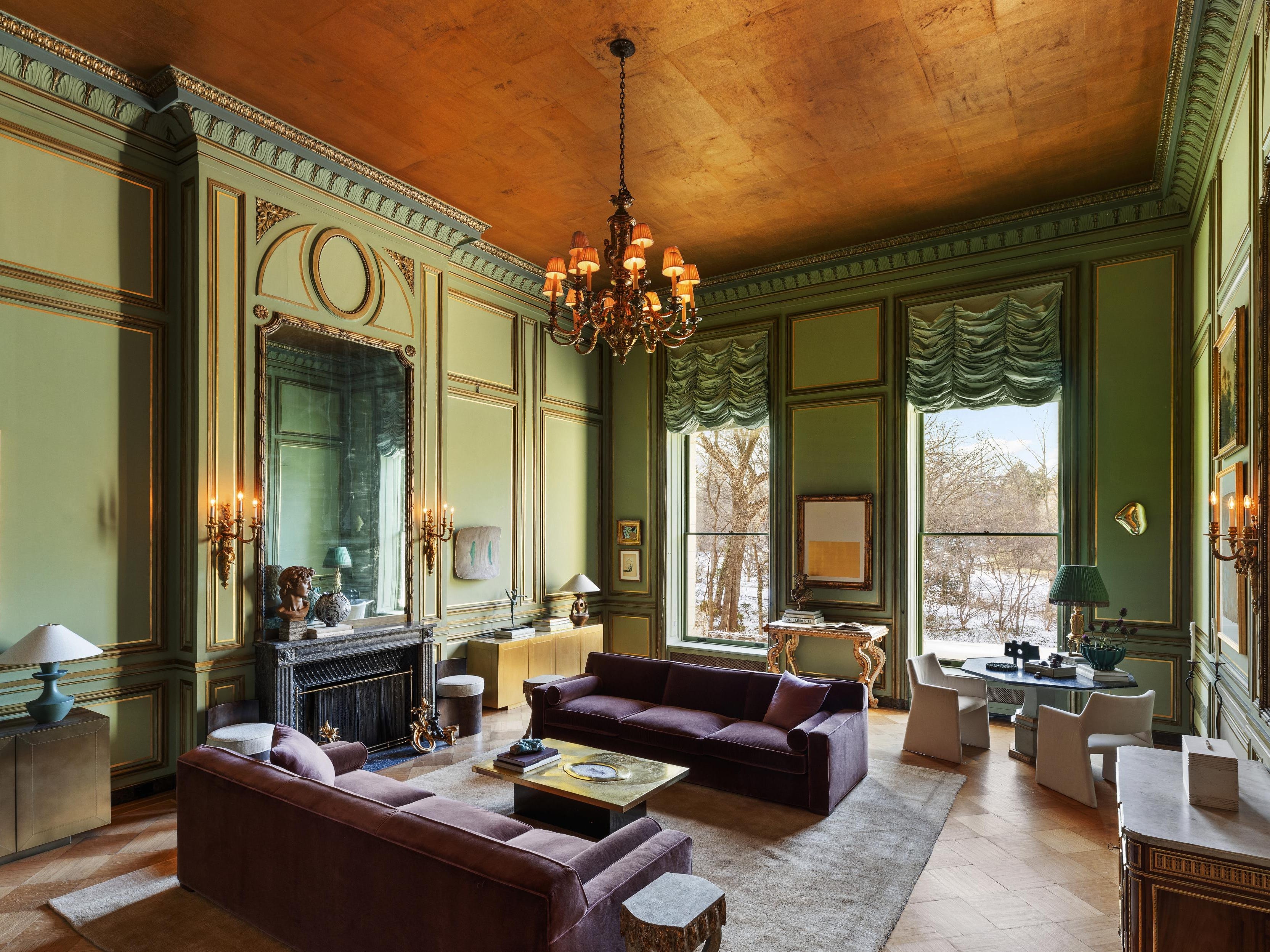 a parlor with green molded walls and large windows overlooking the park