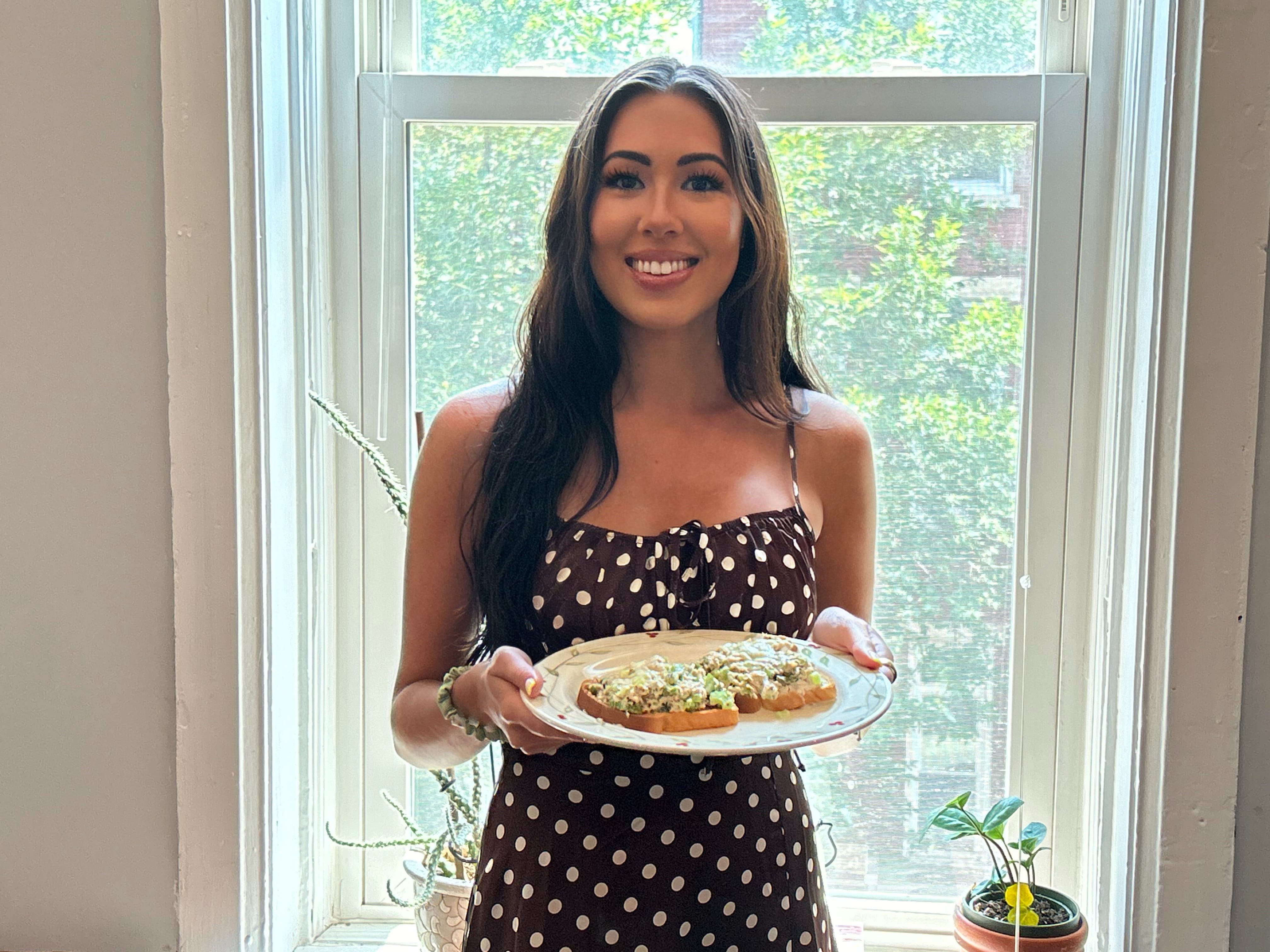 Lara standing in front of a window holding her tuna melt.